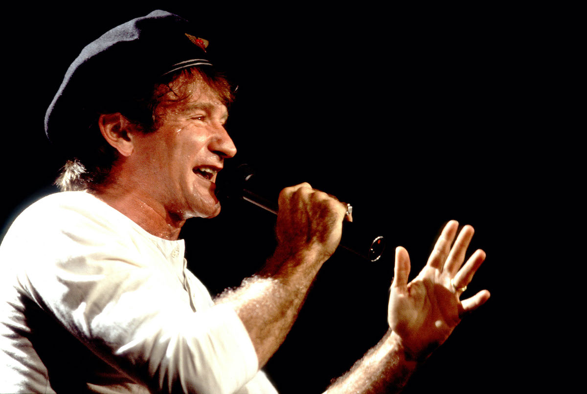 Robin Williams wears a hat and talks into a microphone