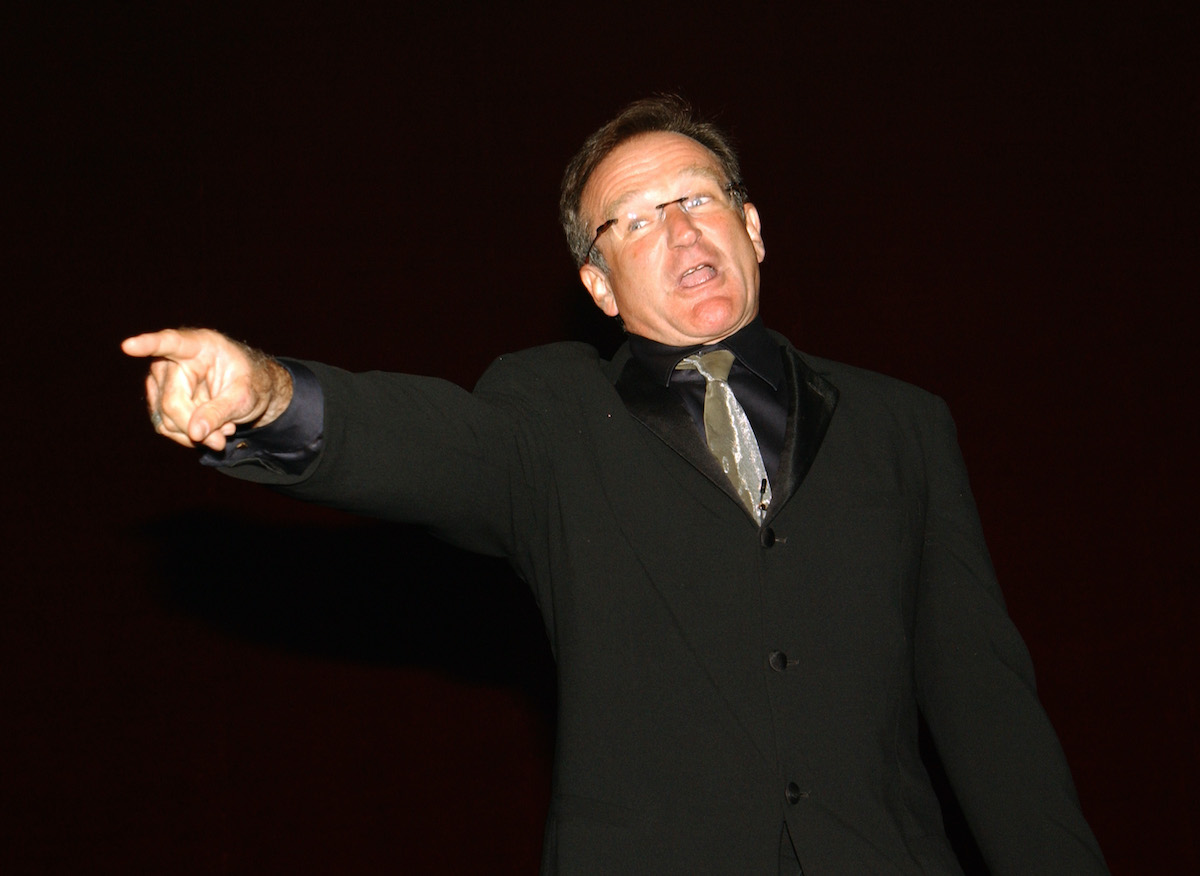 Robin Williams wears a black suit and points