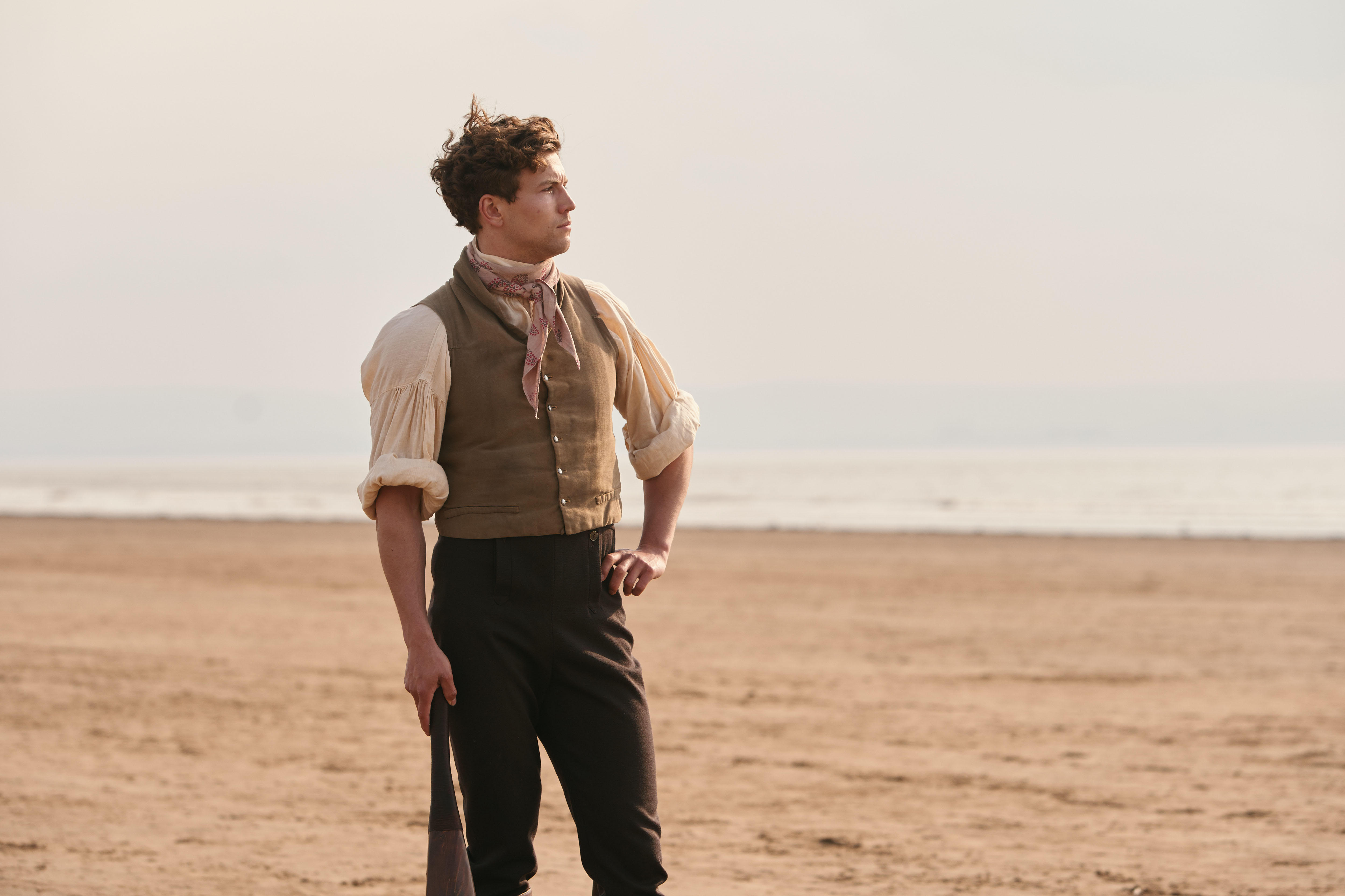 Leo Suter as Young Stringer standing on a beach in 'Sanditon'