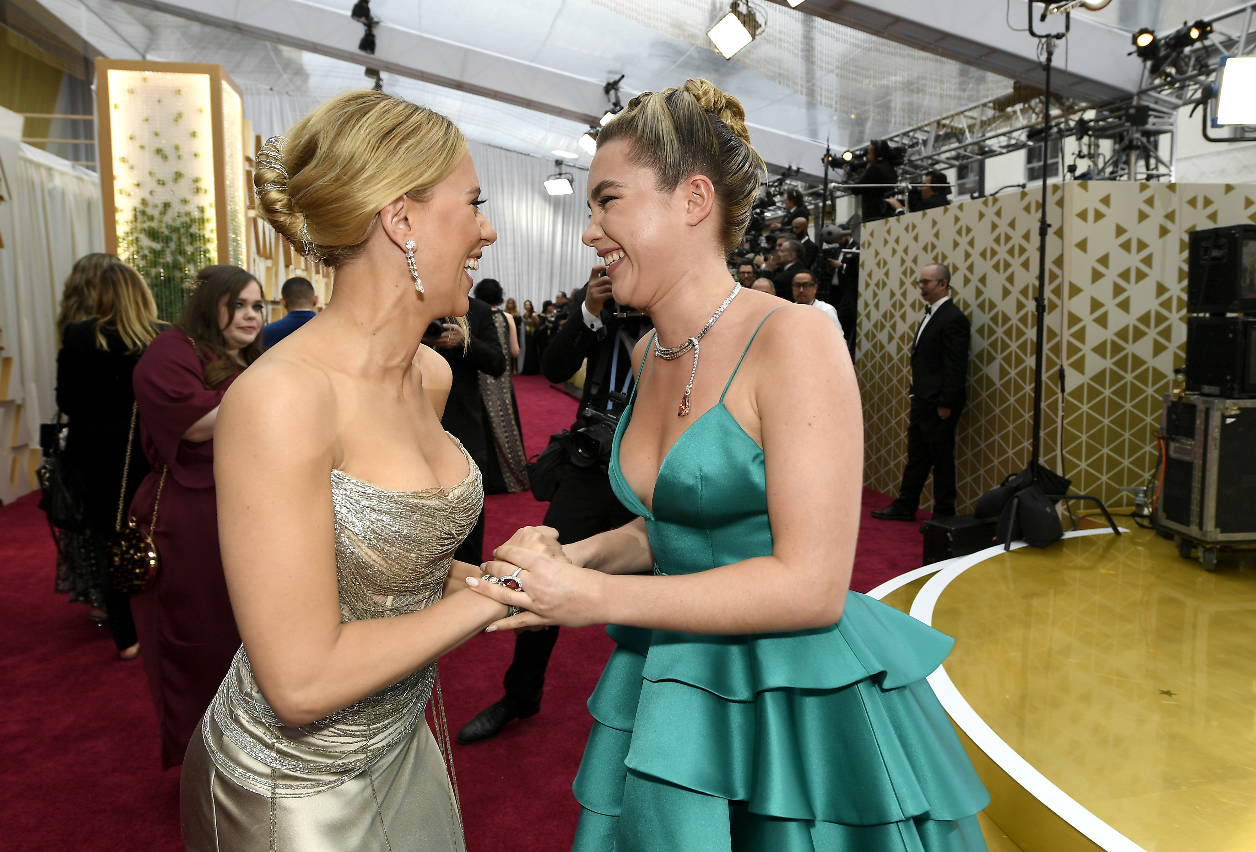 'Black Widow' stars Scarlett Johansson and Florence Pugh smile at one another and hold hands on the red carpet. Johansson wears a strapless sparkly silver dress. Pugh wears a teal dress.