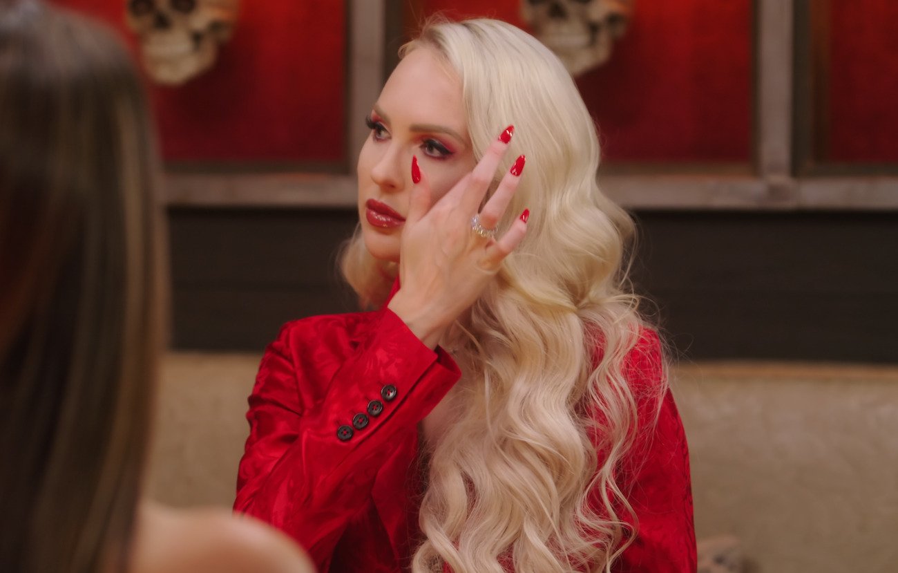 Christine Quinn wearing a red outfit and red nail polish, touching her hair during a scene from 'Selling Sunset'