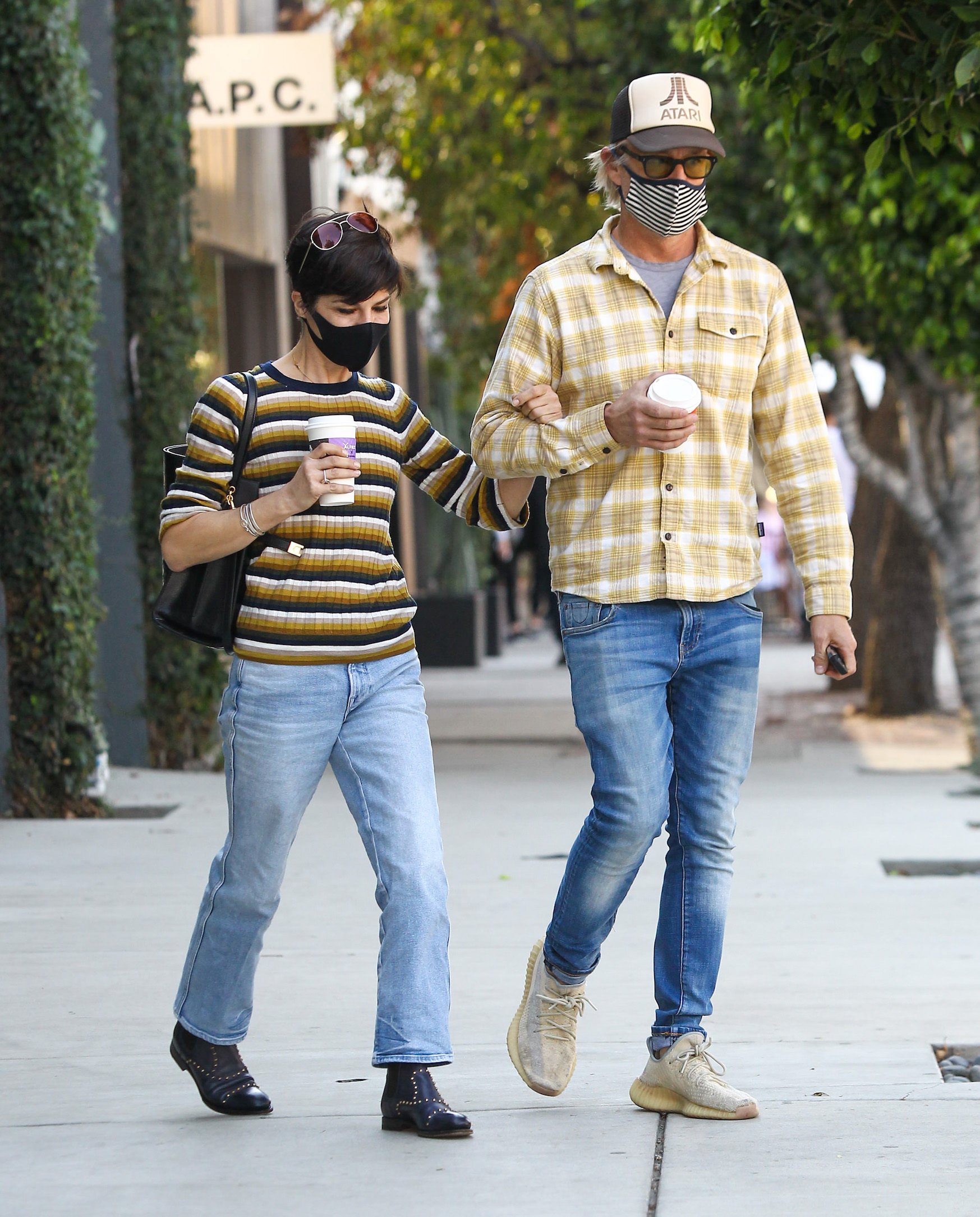 Selma Blair and Ron Carlson walking together outside with coffee in their hands