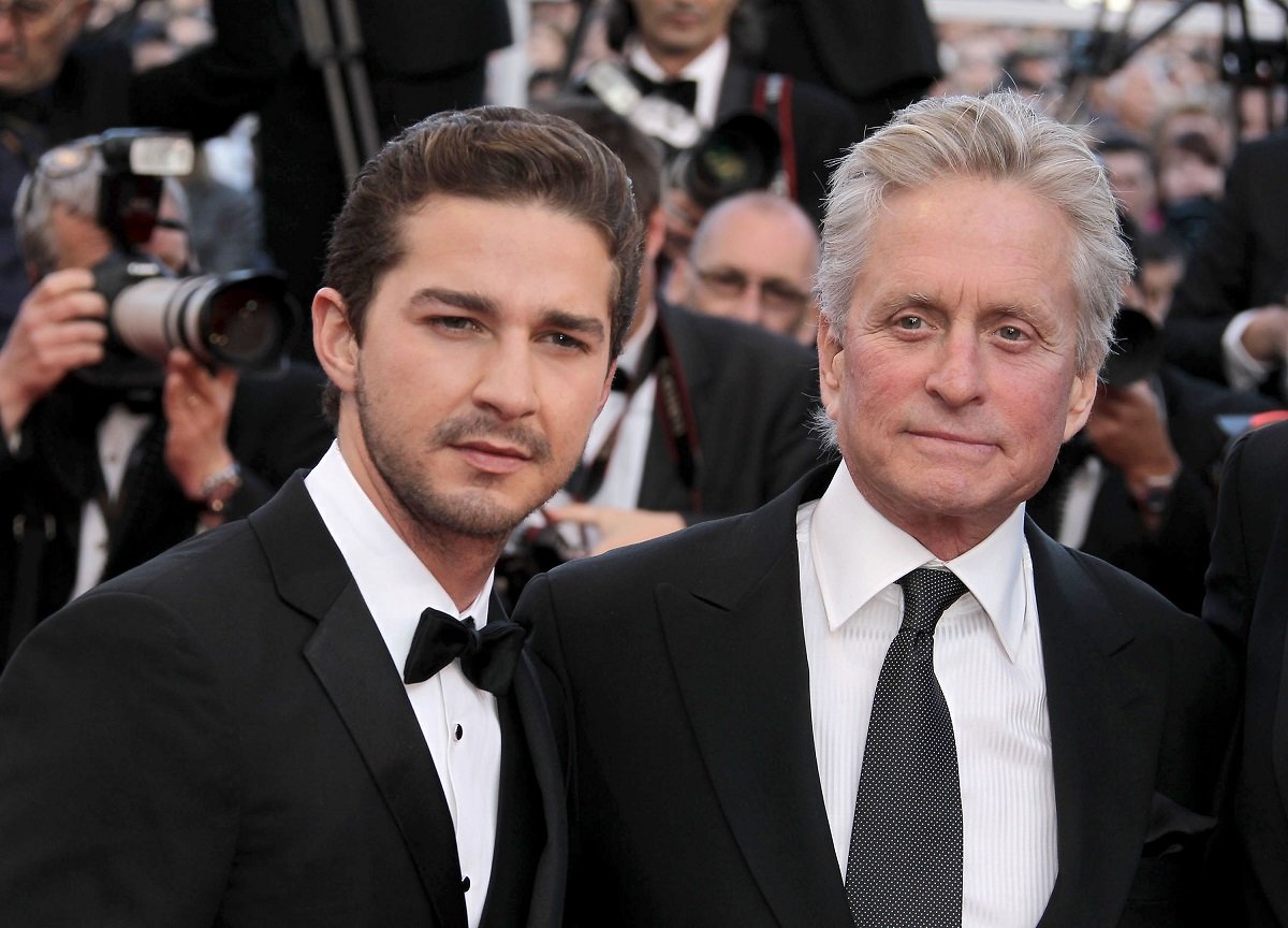 Shia LaBeouf smiling with Michael Douglas while wearing a suit.