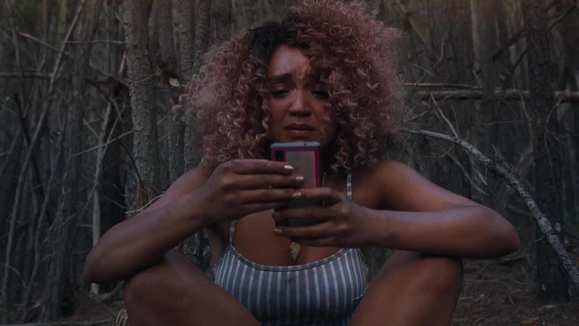 'Sissy' Aisha Dee as Cecilia looking on her cell phone looking worried with bare tree branches behind her