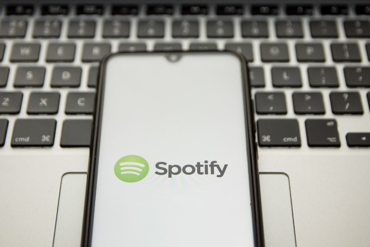 A Spotify logo is seen displayed on a smartphone screen with a computer keyword in the background