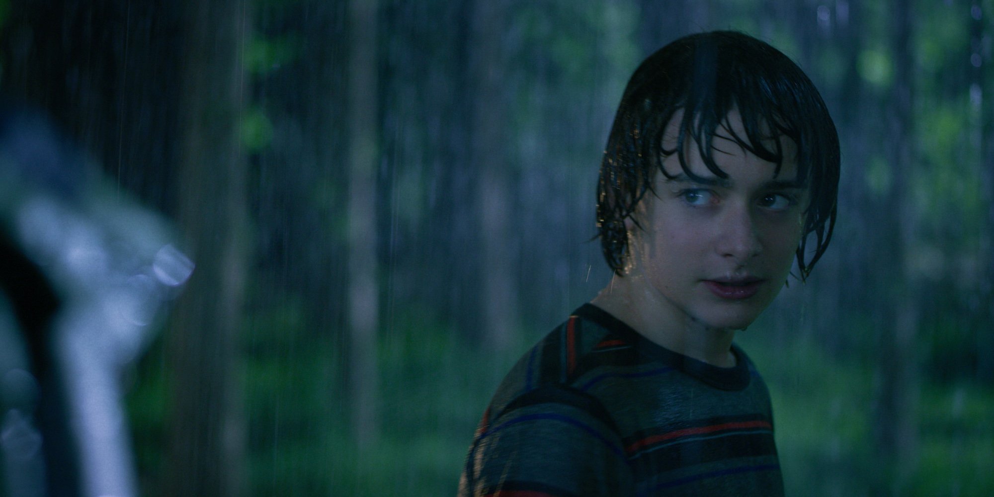 'Stranger Things' star Noah Schnapp standing in the rain in a production still from season 3