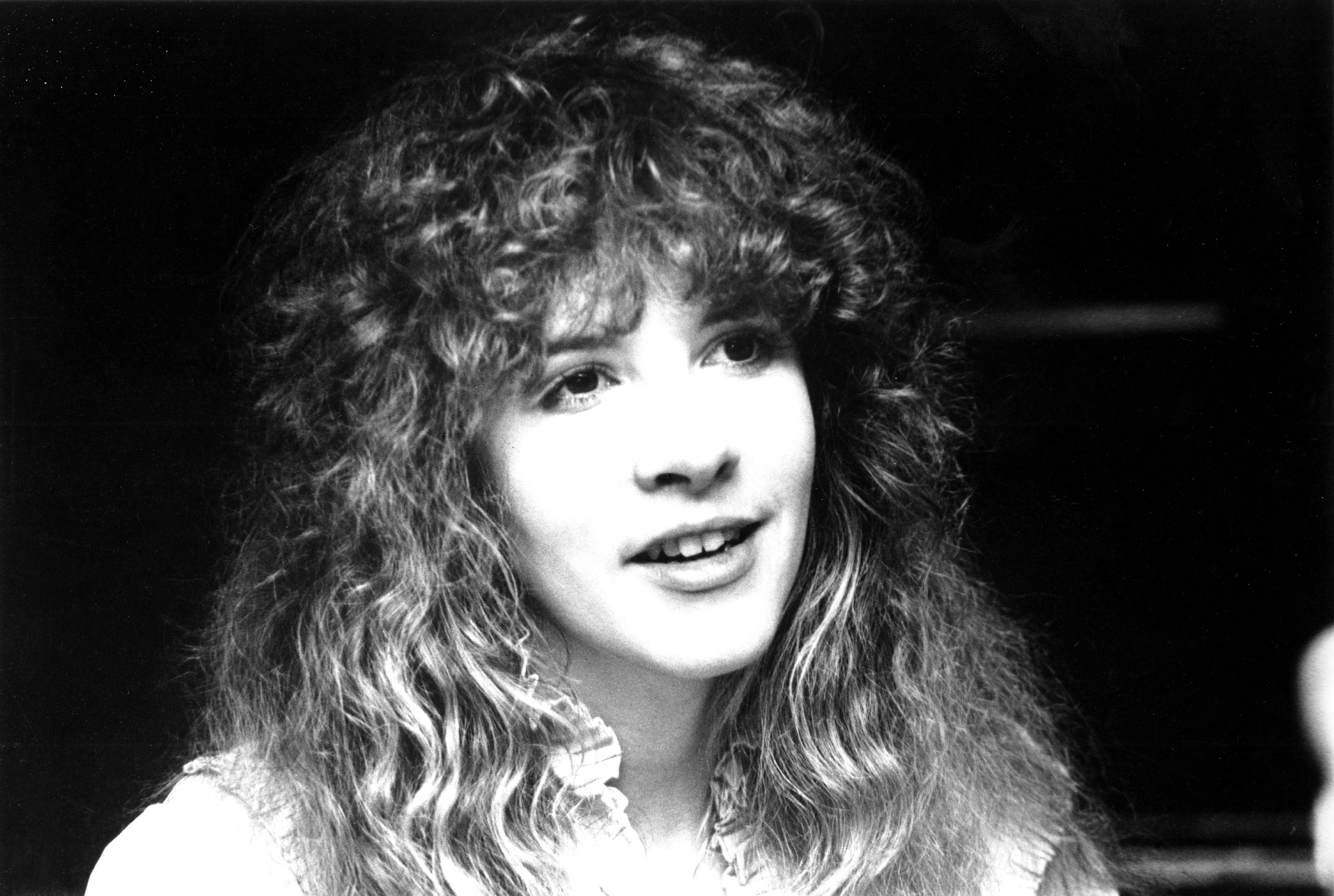 A black and white photo of Stevie Nicks wearing a ruffled white shirt.