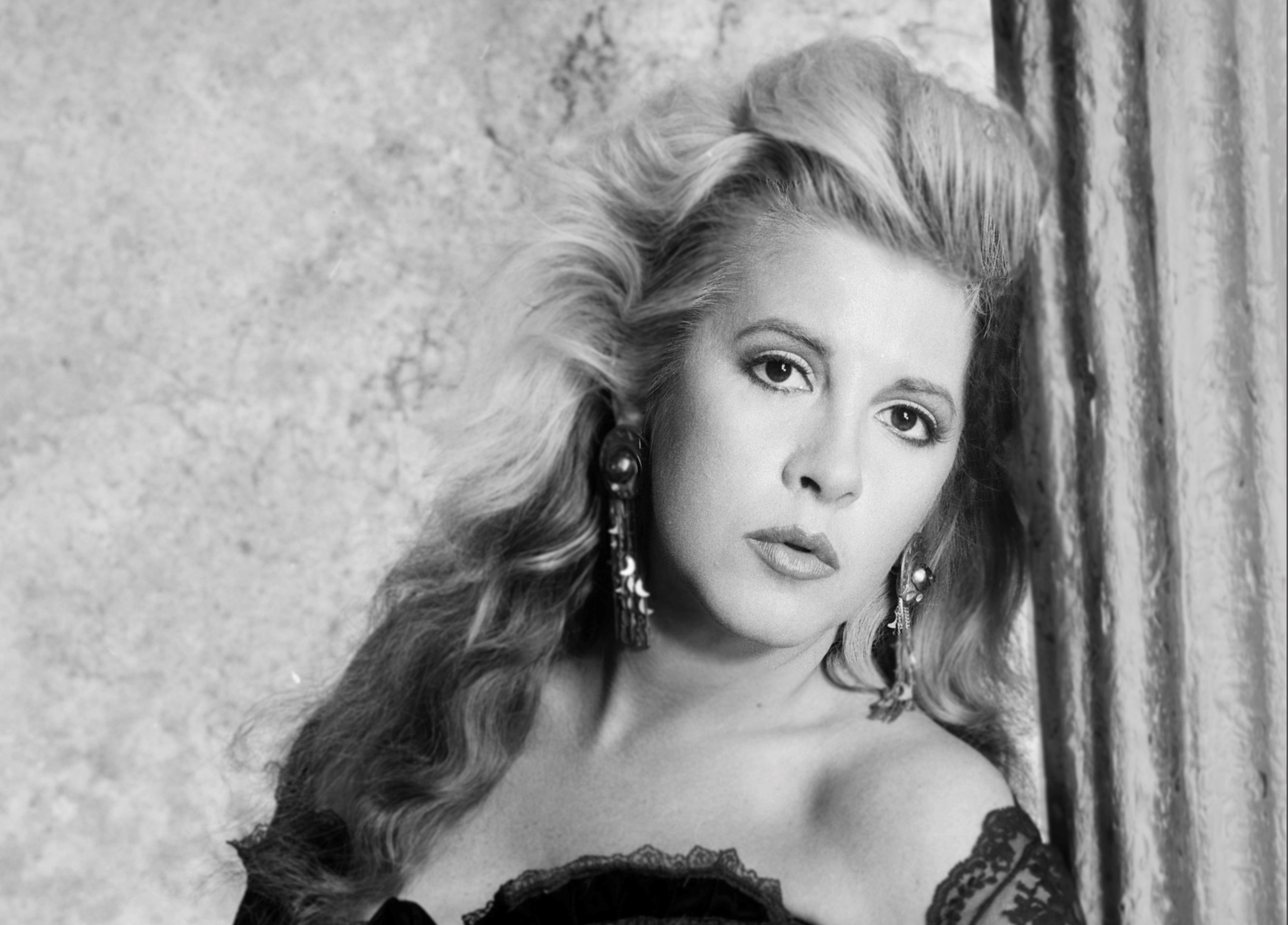 A black and white picture of Stevie Nicks wearing a lace shirt and leaning against a pillar.
