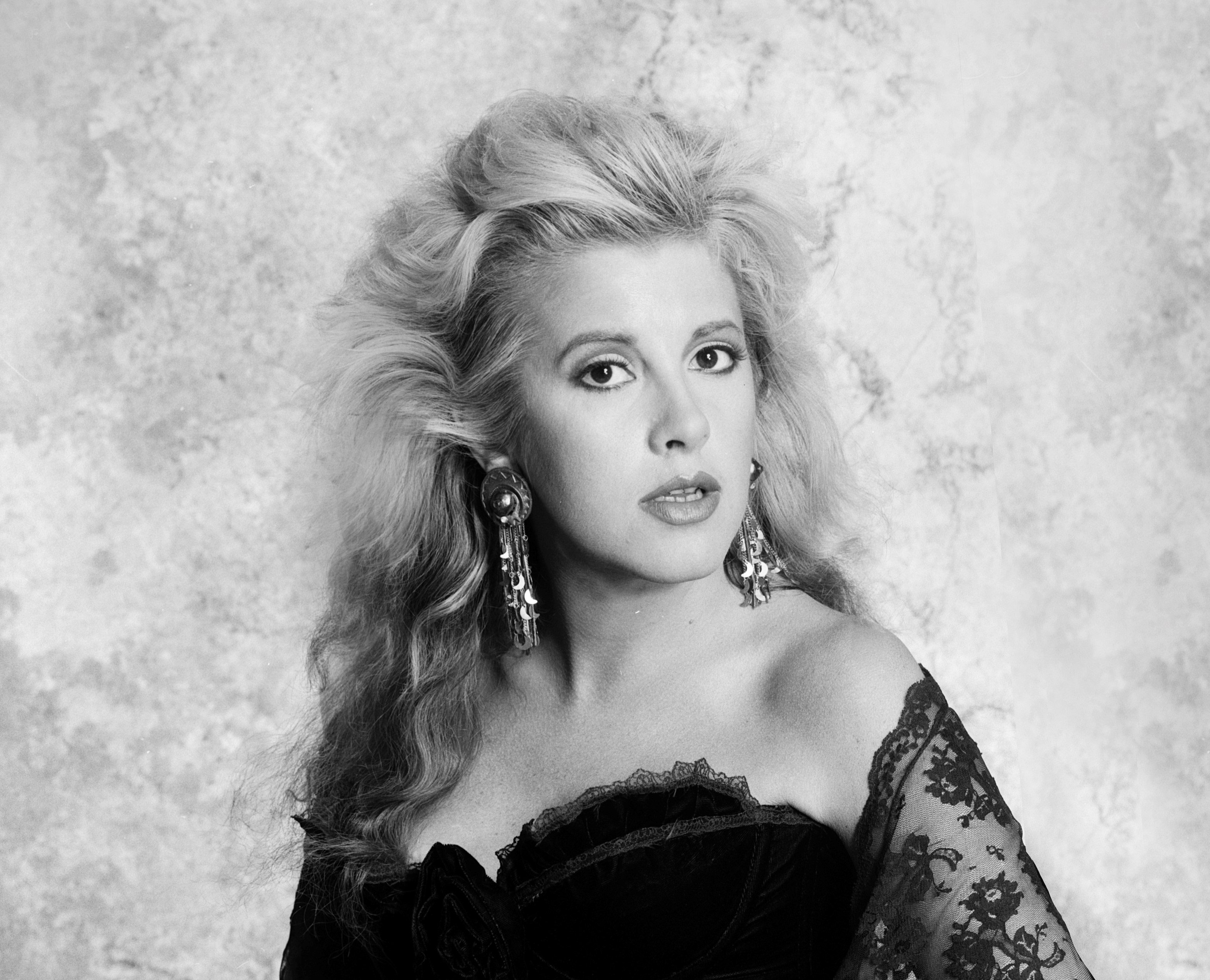 A black and white photo of Stevie Nicks wearing a lace top and dangling earrings.