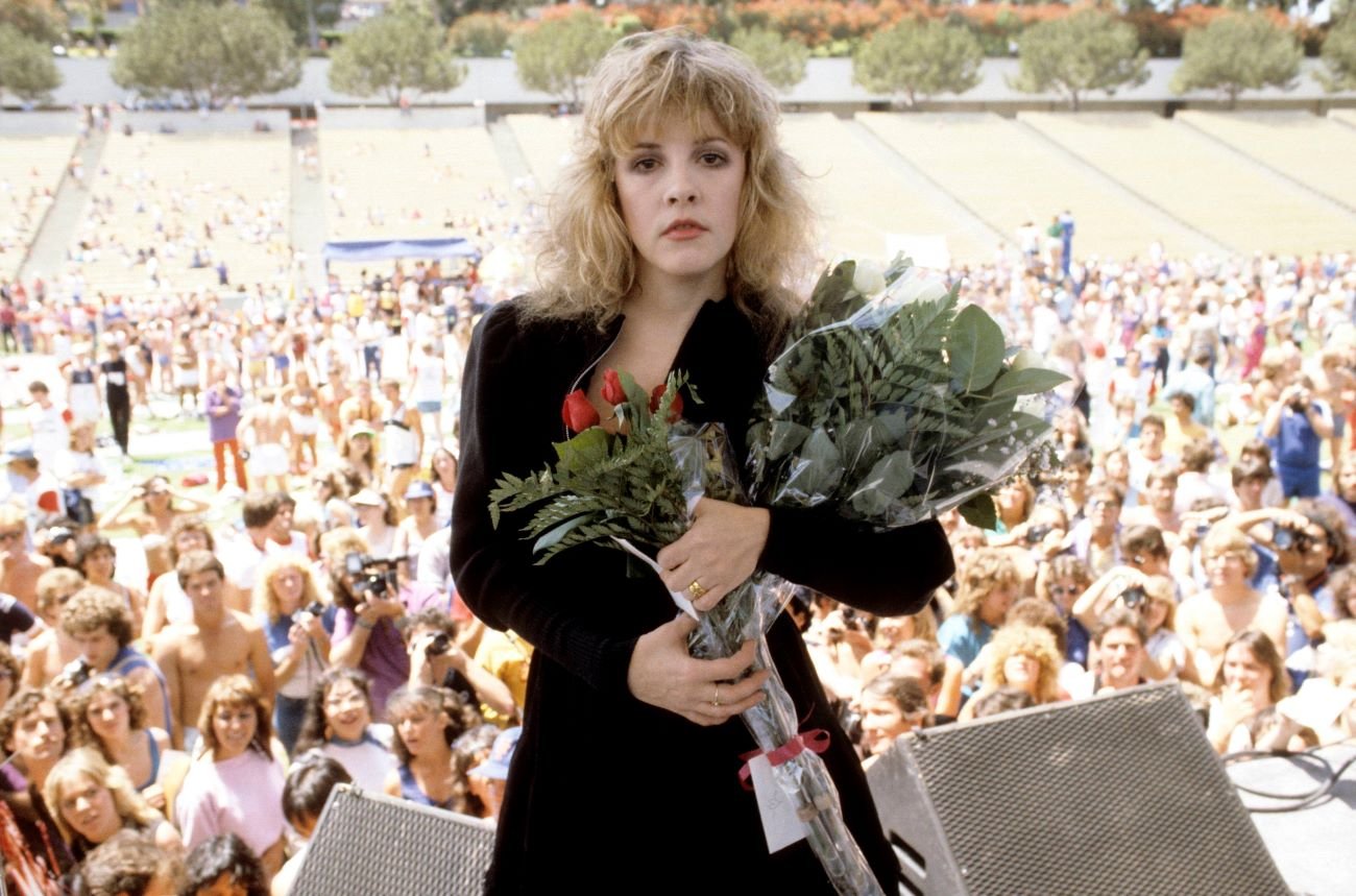 Stevie Nicks stands on stage and holds a bouquet of flowers.