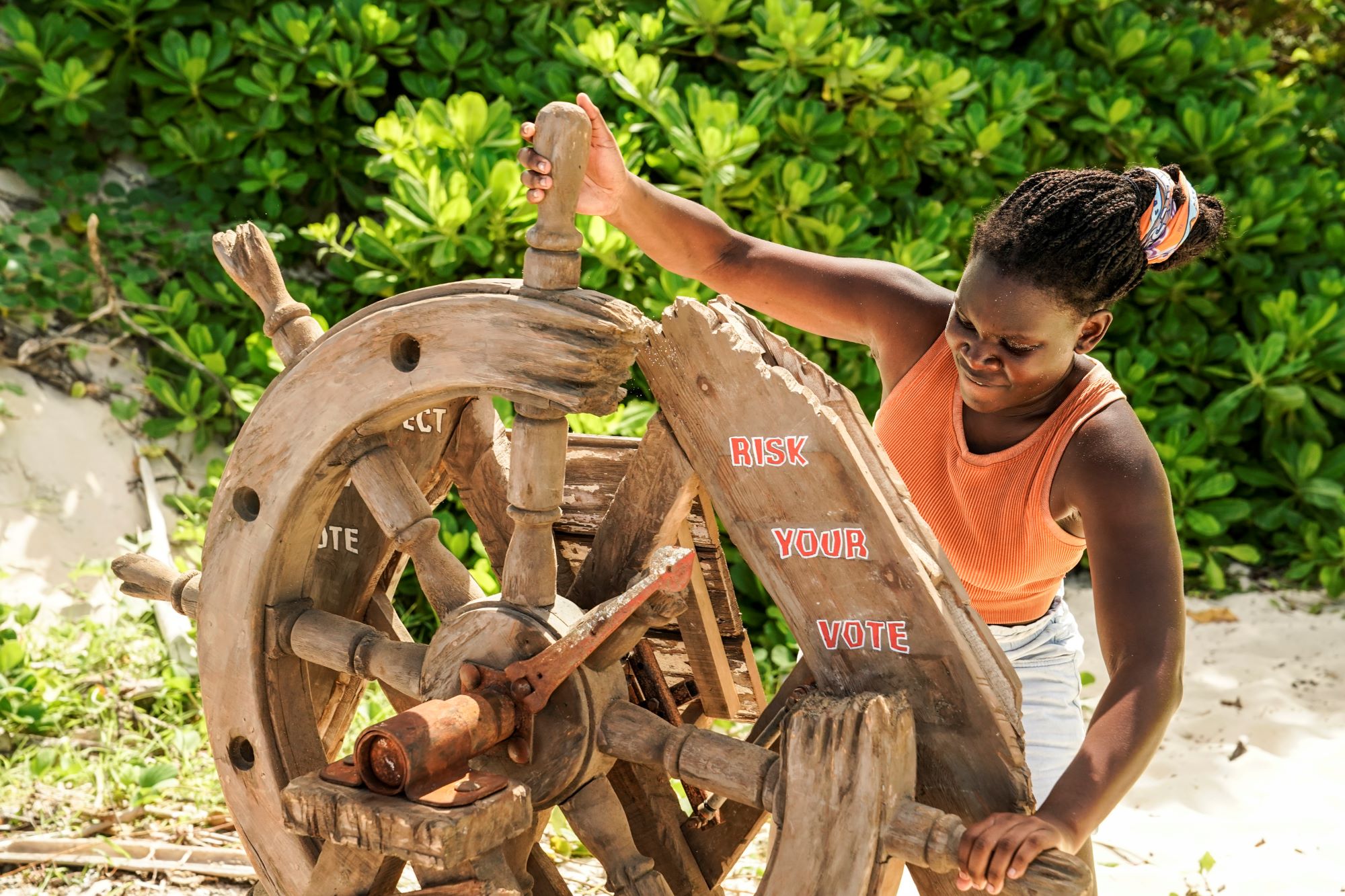 Maryanne Oketch, who some believe is the 'Survivor' Season 42 winner, turns a wheel while wearing an orange tank top, white shorts, and her orange buff in her hair.
