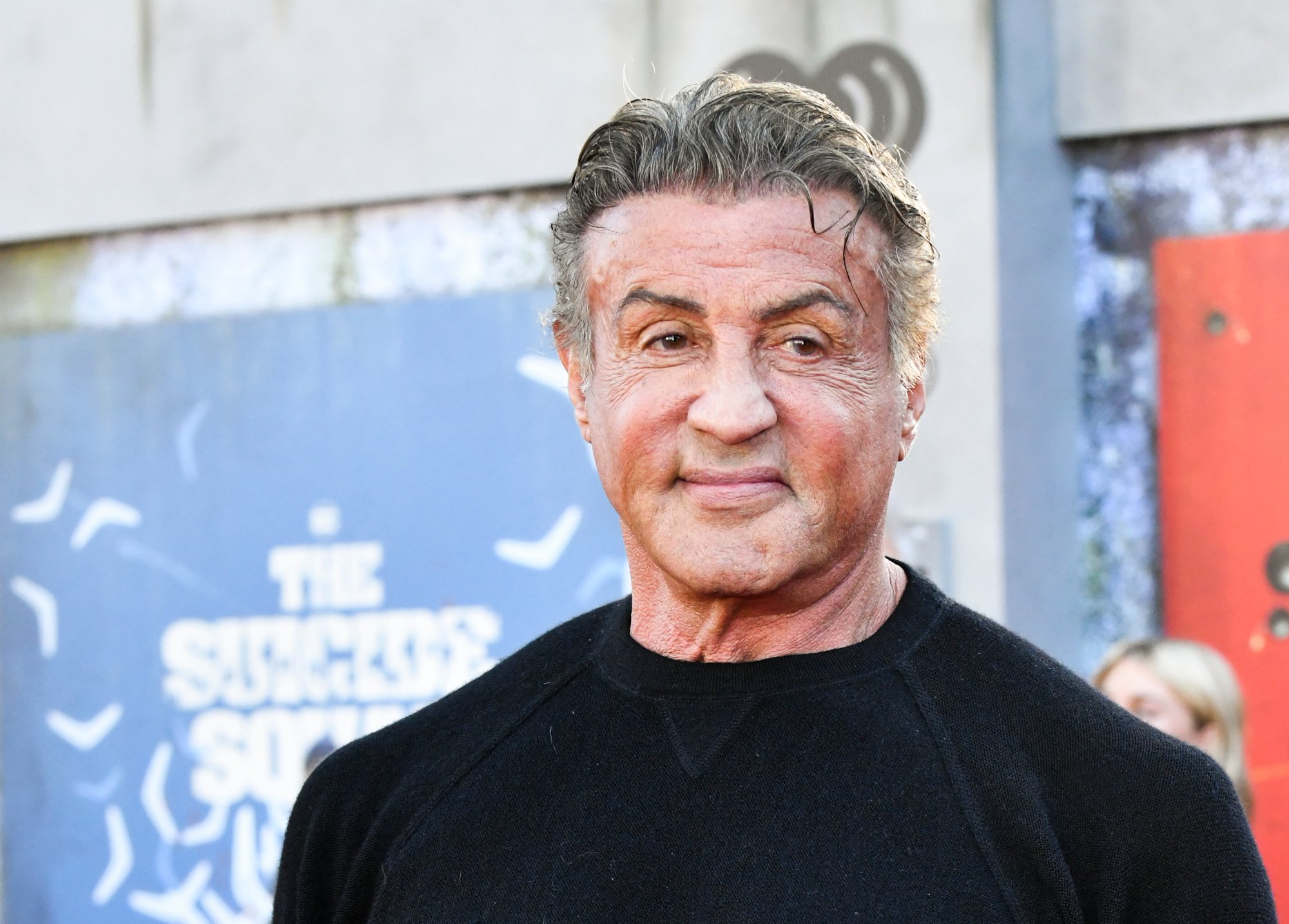 King Shark voice actor Sylvester Stallone at the premiere for 'The Suicide Squad.' He's wearing a black shirt and smiling at the camera.