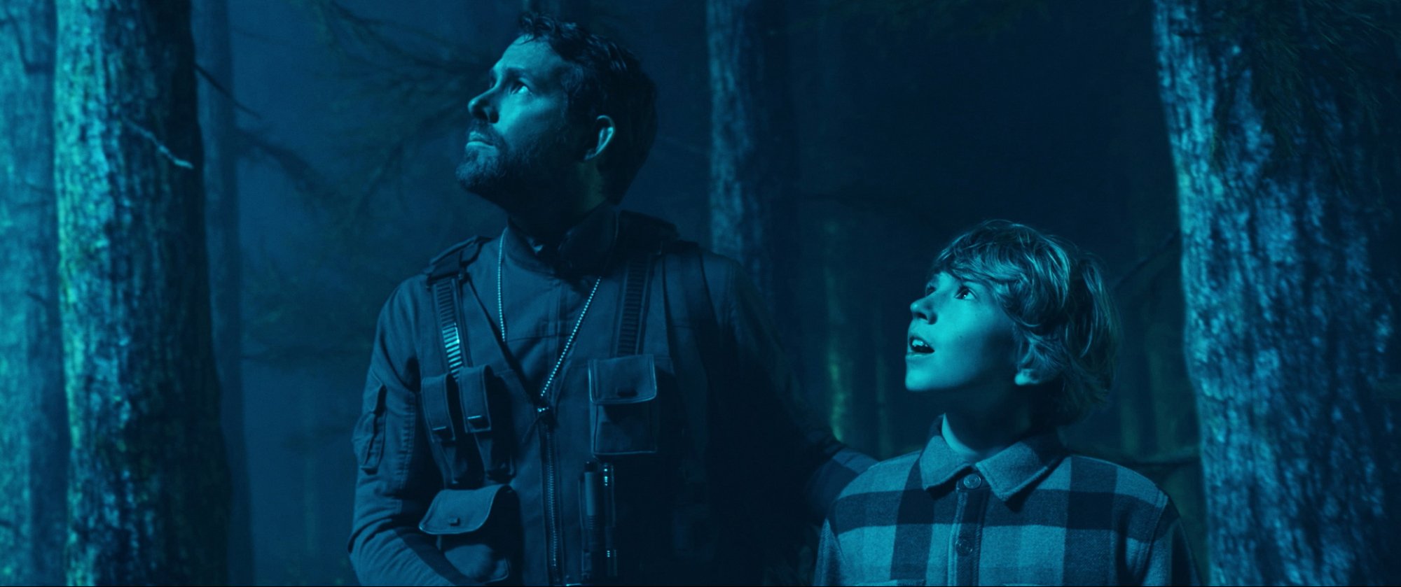 'The Adam Project' Ryan Reynolds as Big Adam and Walker Scobell as Young Adam looking up at blue light in the forest