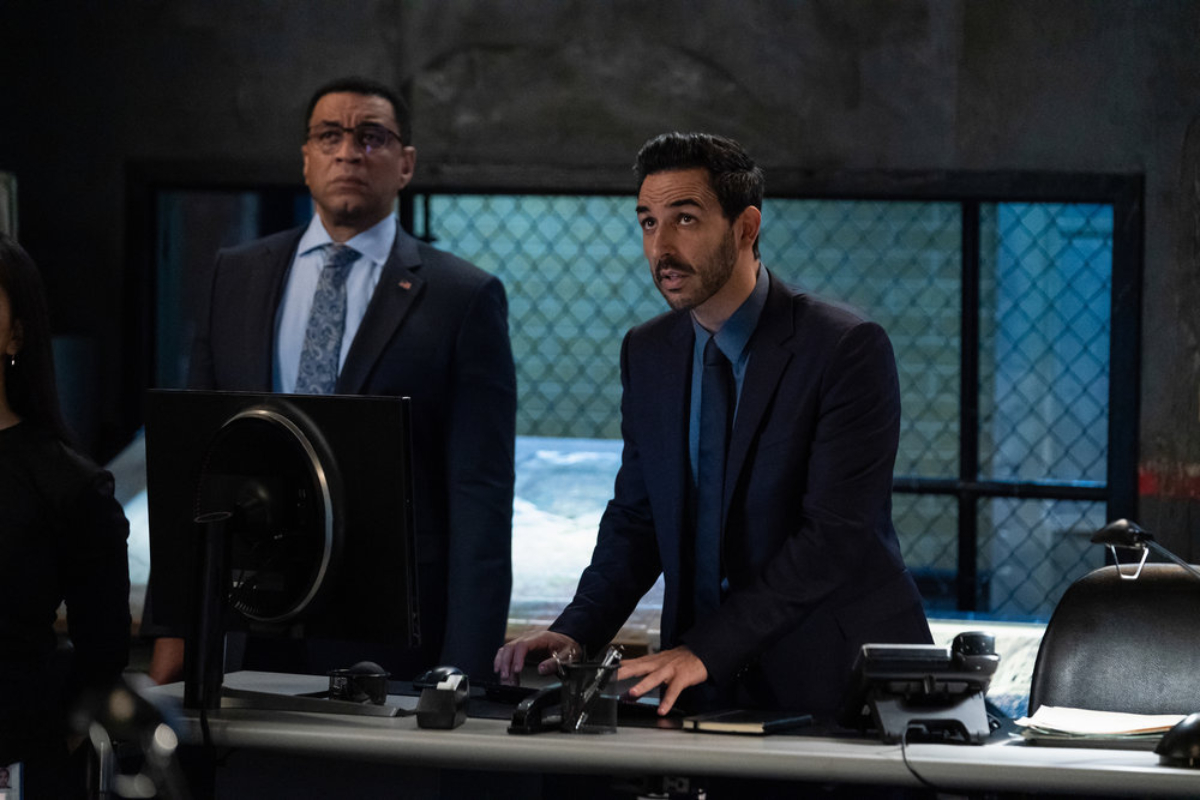 Harry Lennix as Harold Cooper and Amir Arison as Aram Motajabi in The Blacklist Season 9. Cooper and Aram stand behind a desk looking up at something.