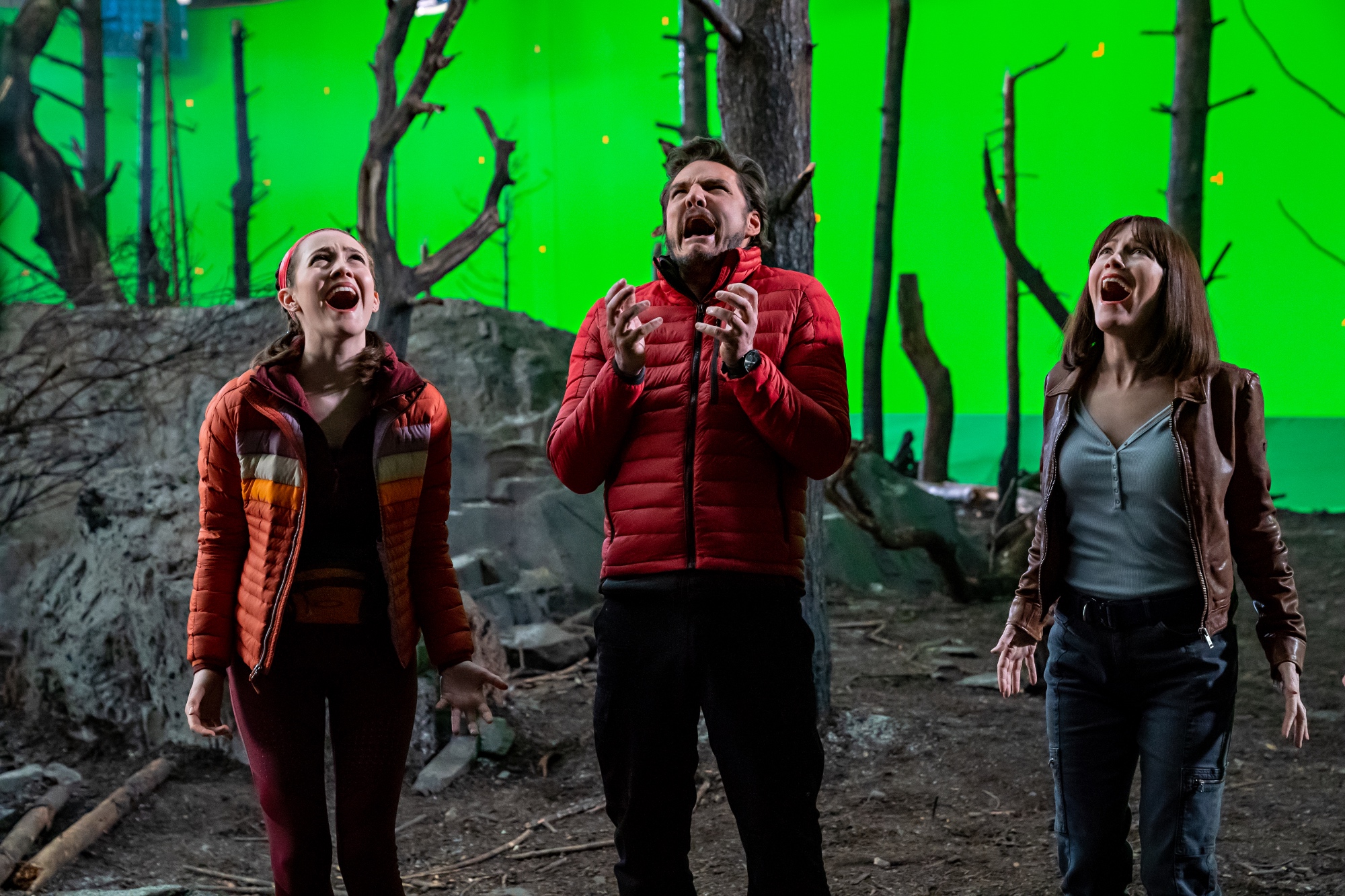 'The Bubble' cast Iris Apatow as Krystal Kris, Pedro Pascal as Dieter Bravo, and Leslie Mann as Lauren Van Chance screaming on a forest movie set with a green screen behind them