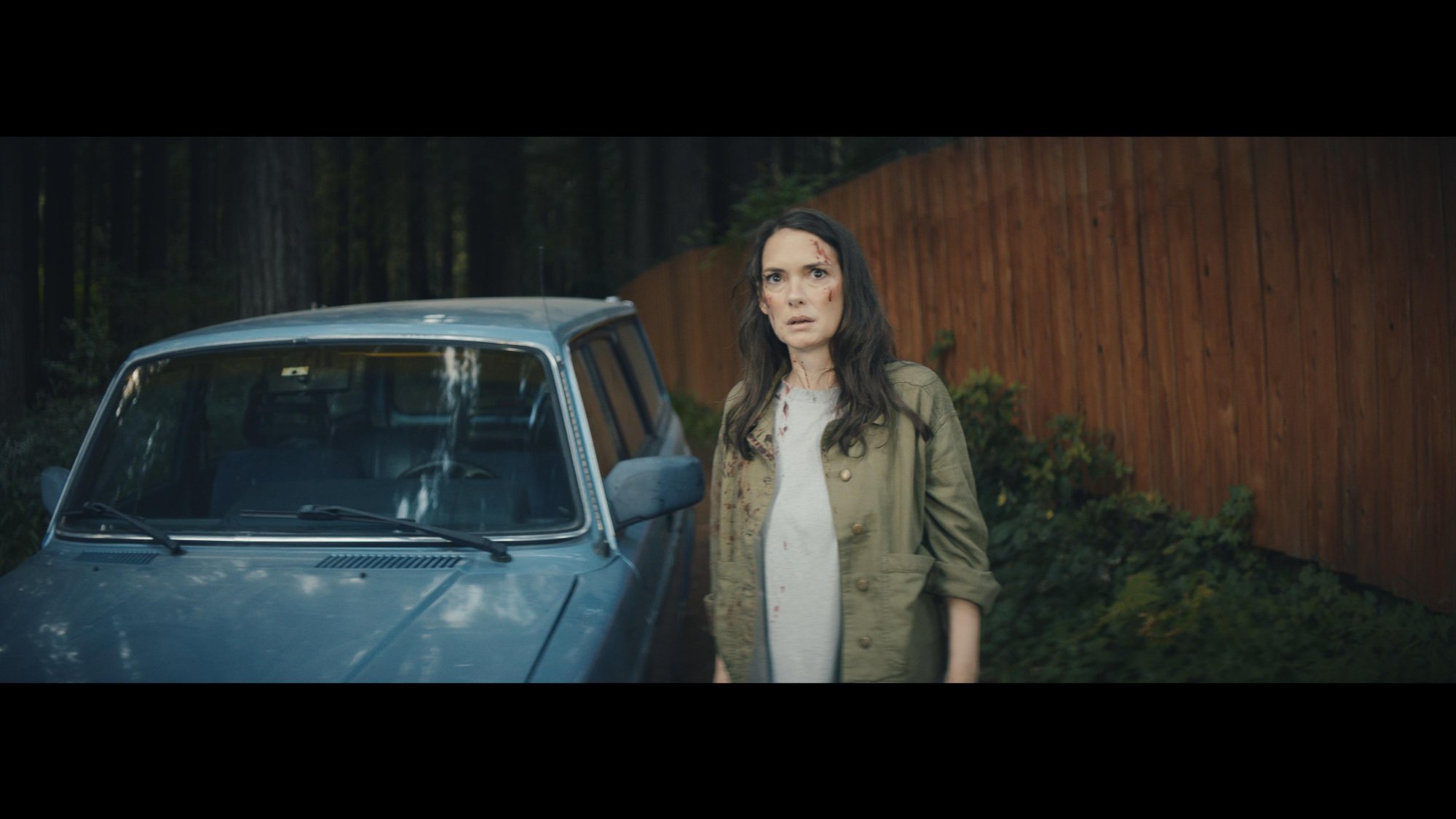 'The Cow' Winona Ryder as Kath with blood on her face walking next to a parked car