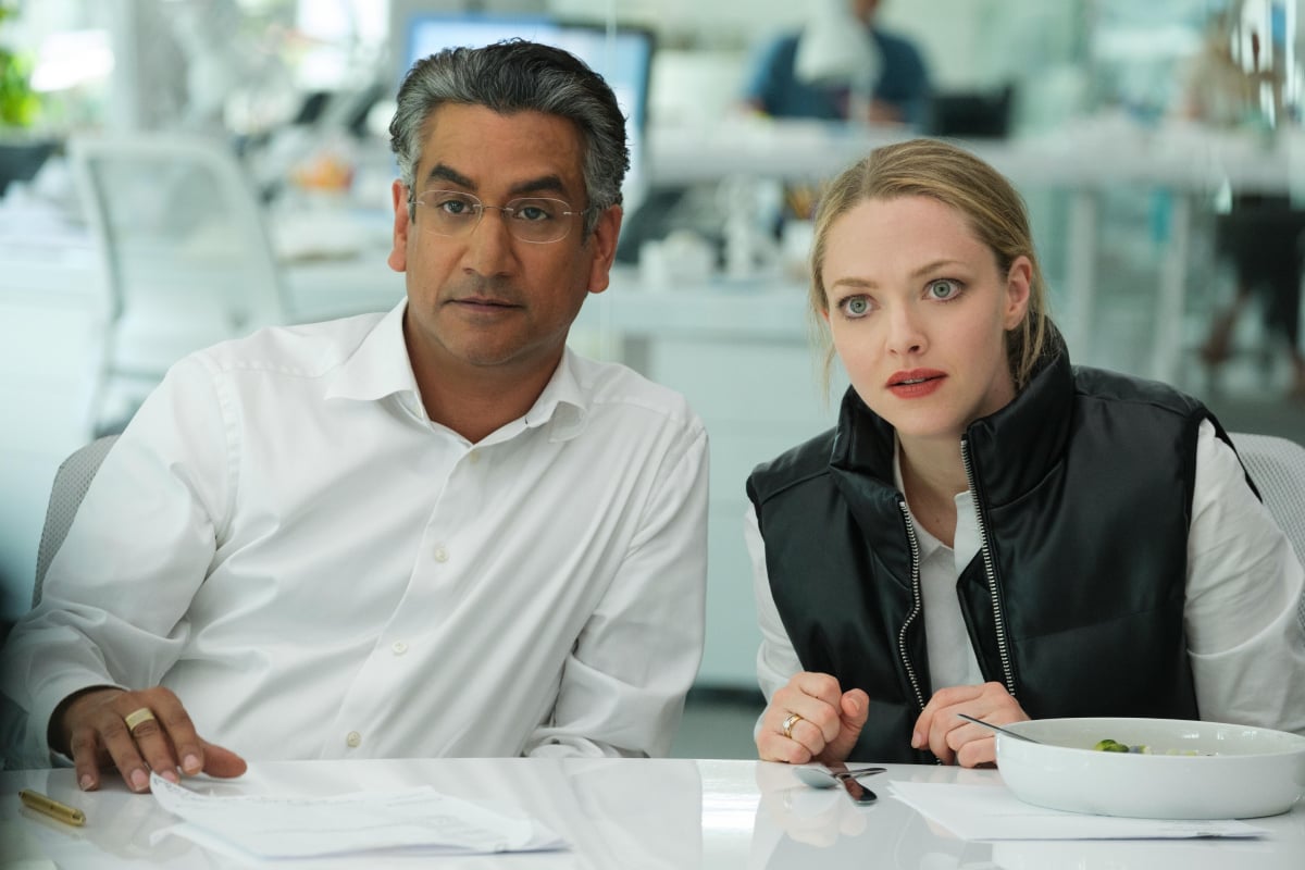 Naveen Andrews as Sunny Balwani and Amanda Seyfried as Elizabeth Holmes in The Dropout. Sunny and Elizabeth are sitting at a desk. 