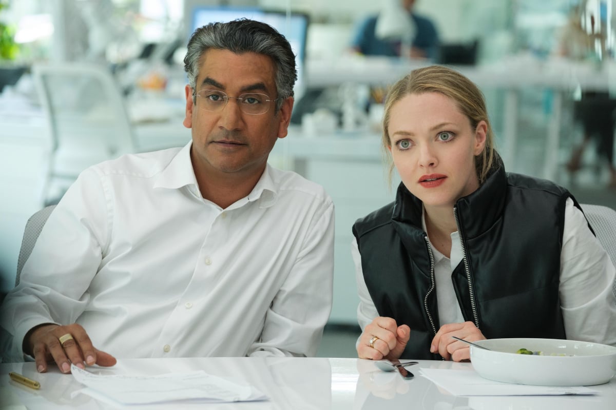 Naveen Andrews as Sunny Balwani and Amanda Seyfried as Elizabeth Holmes in The Dropout. Sunny and Elizabeth are sitting at a desk.