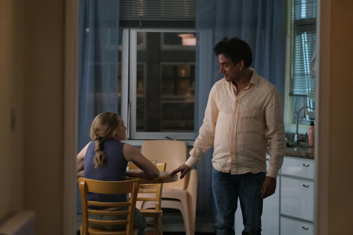 Amanda Seyfried as Elizabeth Holmes and Naveen Andrews as Sunny Balwani in The Dropout. Holmes sits at a table and Balwani stands next to her.
