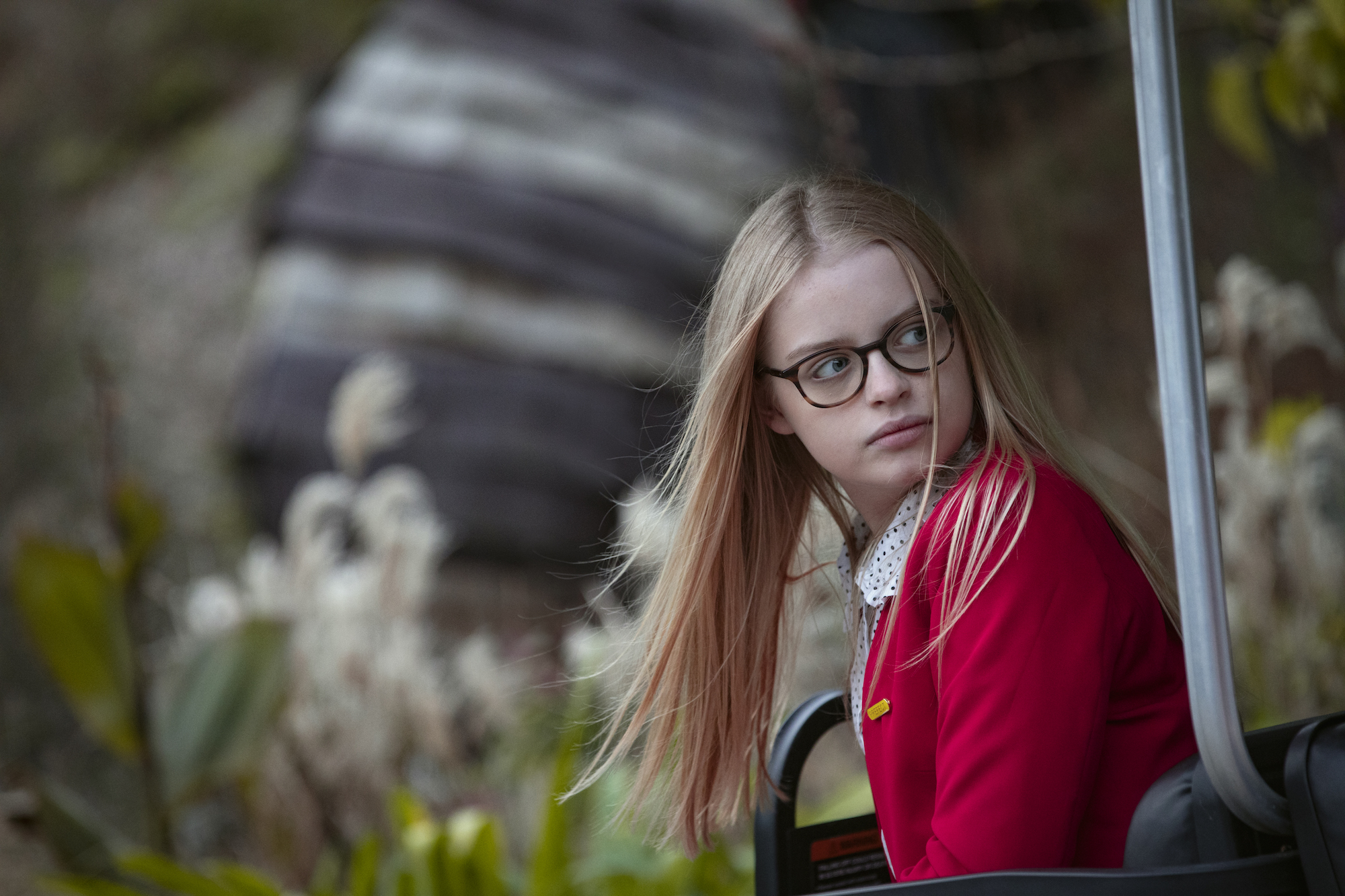 'The Last Bus' starring Robert Sheehan also features Marlie Morelle as Chelsea wearing a red sweater and looking to the side in a production still from season 1.