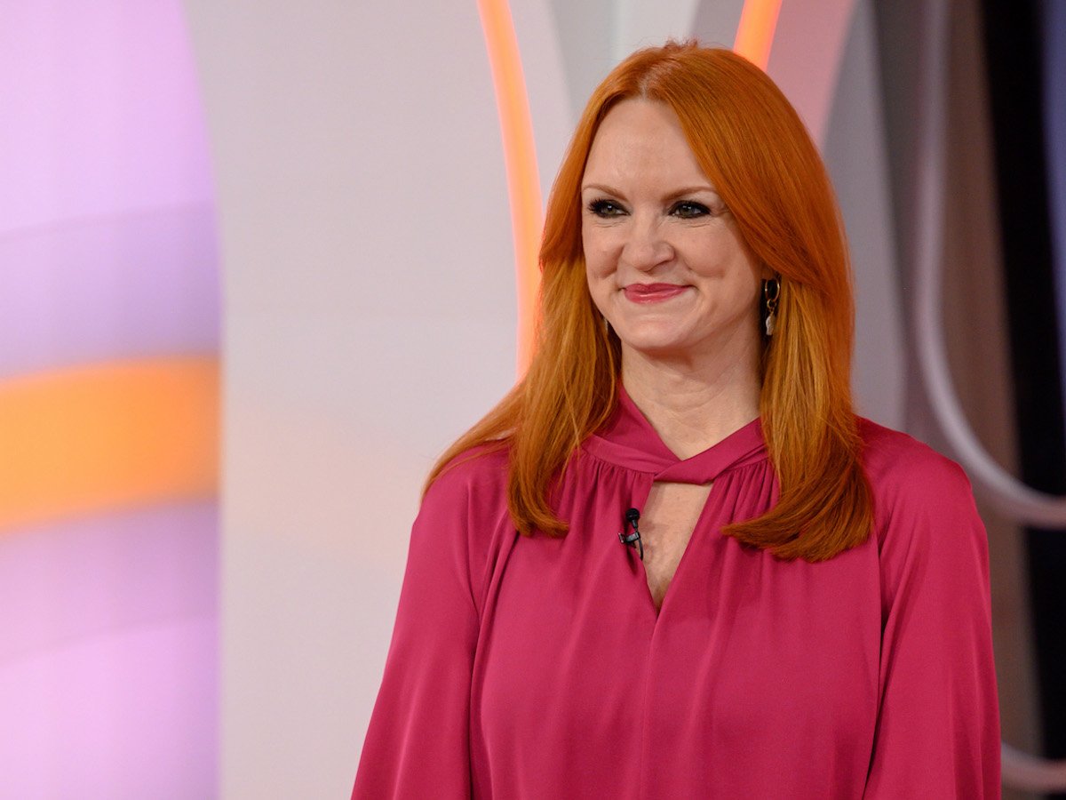 Ree Drummond smirks as she looks on wearing a pink shirt