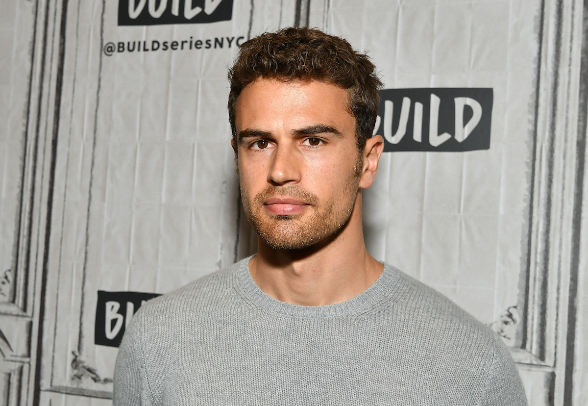 Theo James wears a grey shirt and looks into the camera
