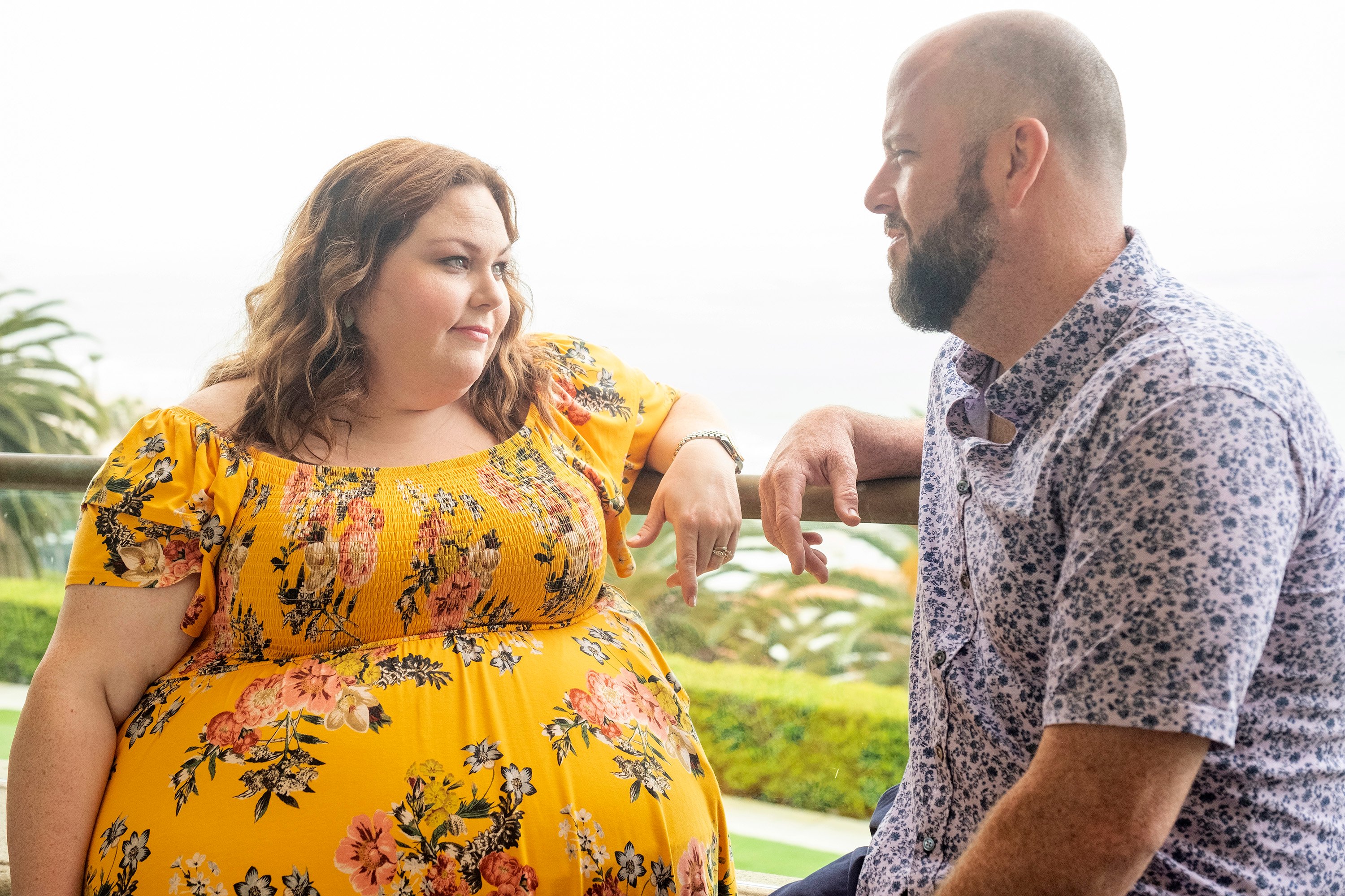 Chrissy Metz and Chris Sullivan, who are a part of the 'This Is Us' cast as Kate and Toby, share a scene. Kate wears a yellow dress with pink and white flowers. Toby wears a blue and white floral short-sleeve button-up shirt.