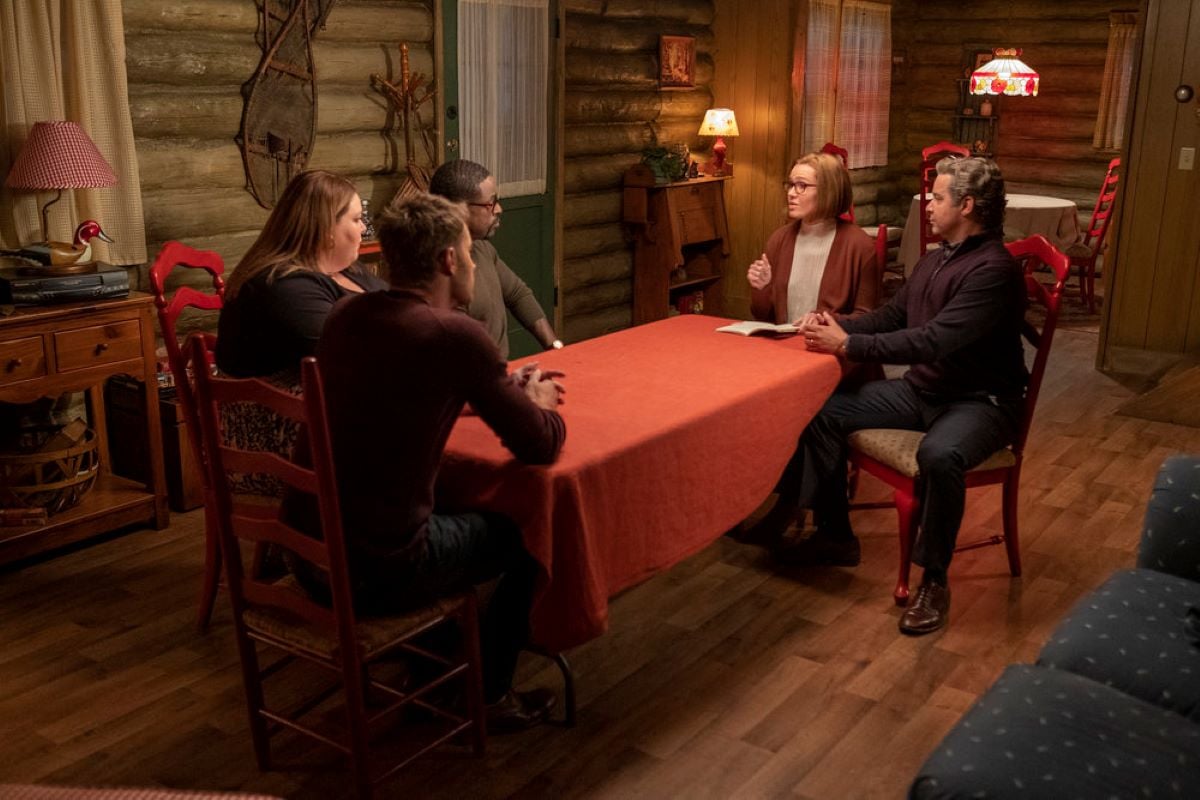 'This Is Us' Season 6 Episode 7 stars Justin Hartley, Chrissy Metz, Sterling K. Brown, Mandy Moore, and Jon Huertas, in character as Kevin, Kate, Randall, Rebecca, and Miguel, gather at a table in the cabin. Kevin, Kate, and Randall sit at one end, while Rebecca and Miguel sit at the other end.