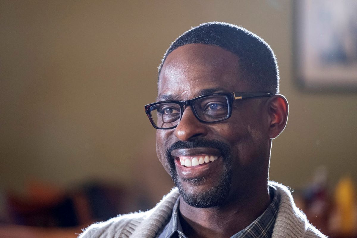 Sterling K. Brown stars as Randall Pearson in 'This Is Us' Season 6 Episode 10, which airs tonight, March 29. Randall wears black-framed glasses, a white cardigan, and a blue plaid button-up shirt.