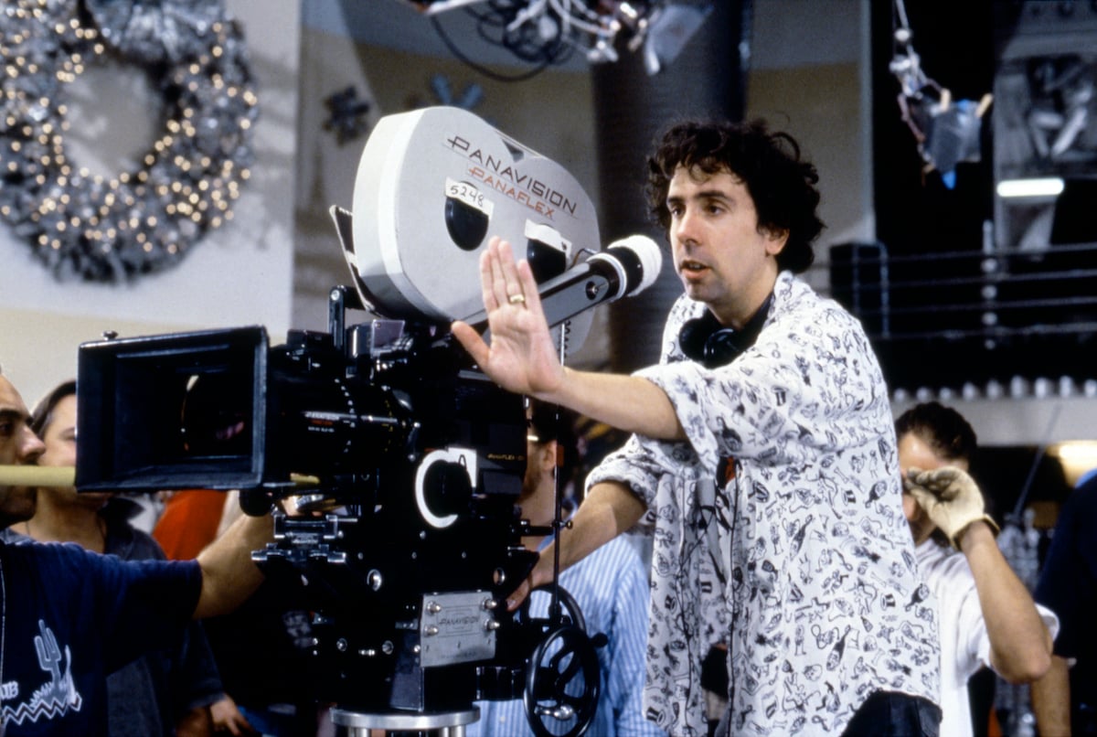Tim Burton stands behind a camera with his hand out on the set of ‘Batman Returns’