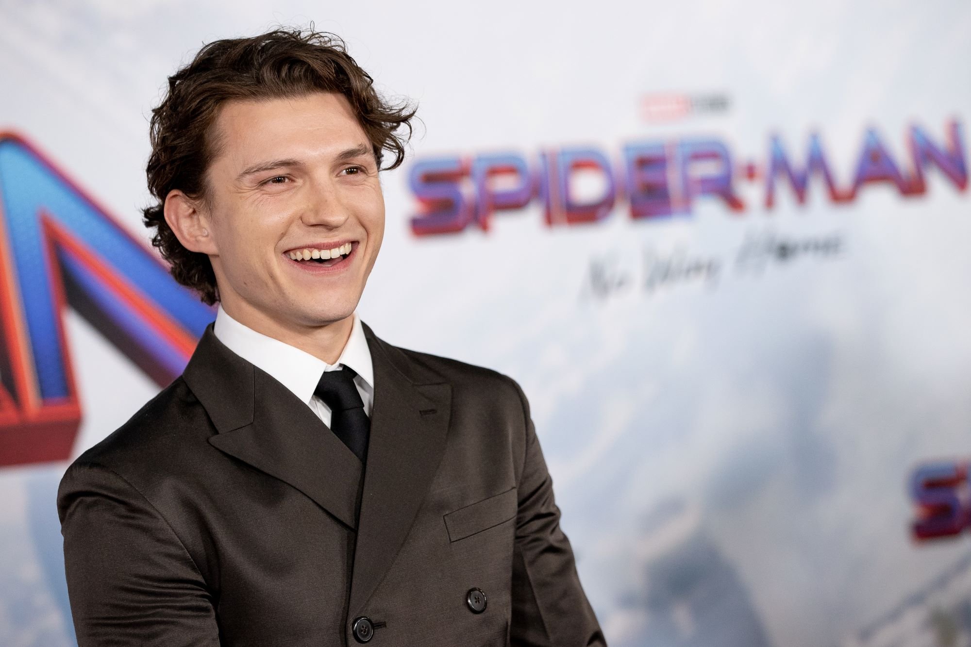 Tom Holland, star of Oscar-nominated film 'Spider-Man: No Way Home,' wears a dark gray suit over a white button-up shirt and black tie.