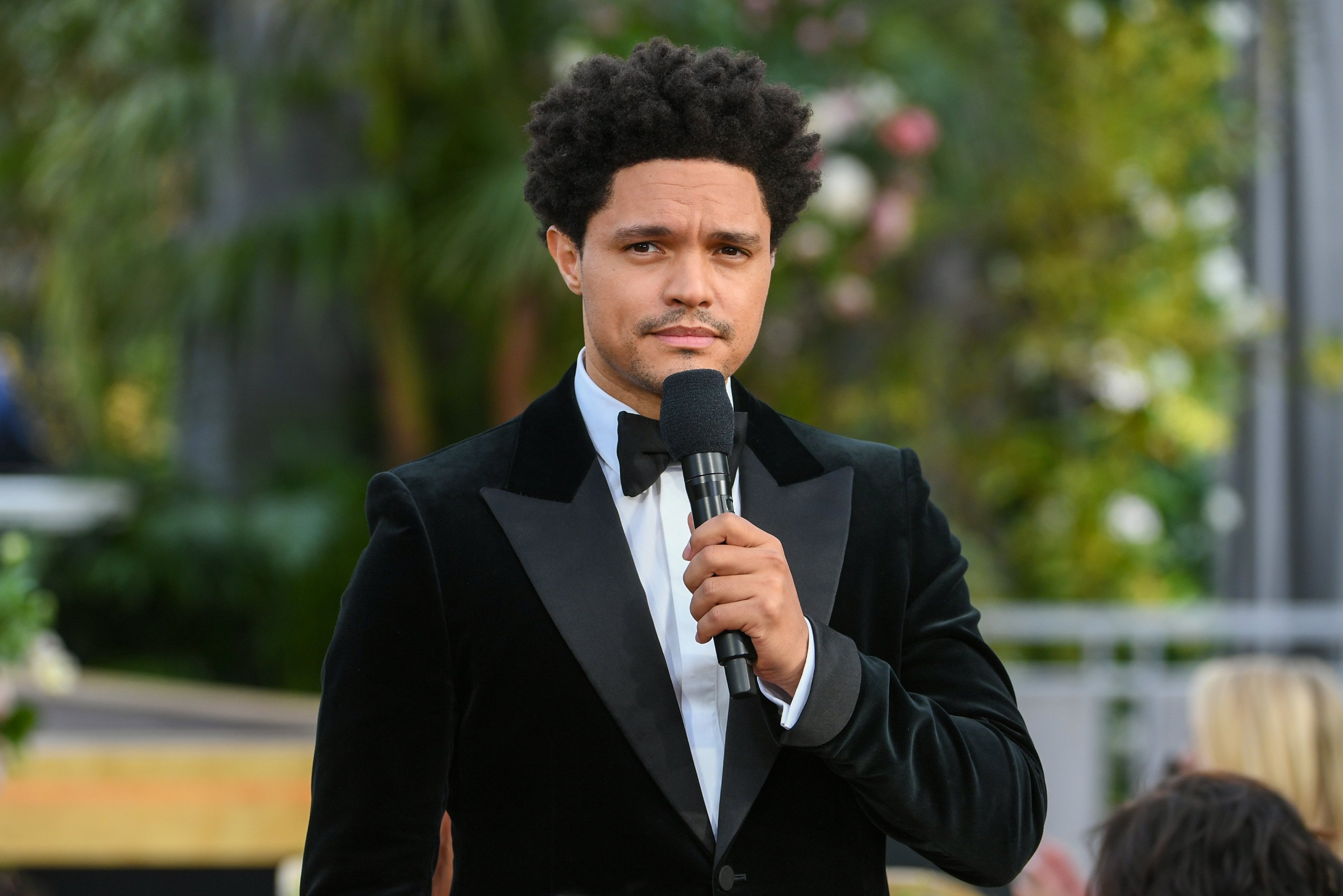 Trevor Noah holds a microphone on stage while hosting the Grammy Awards.