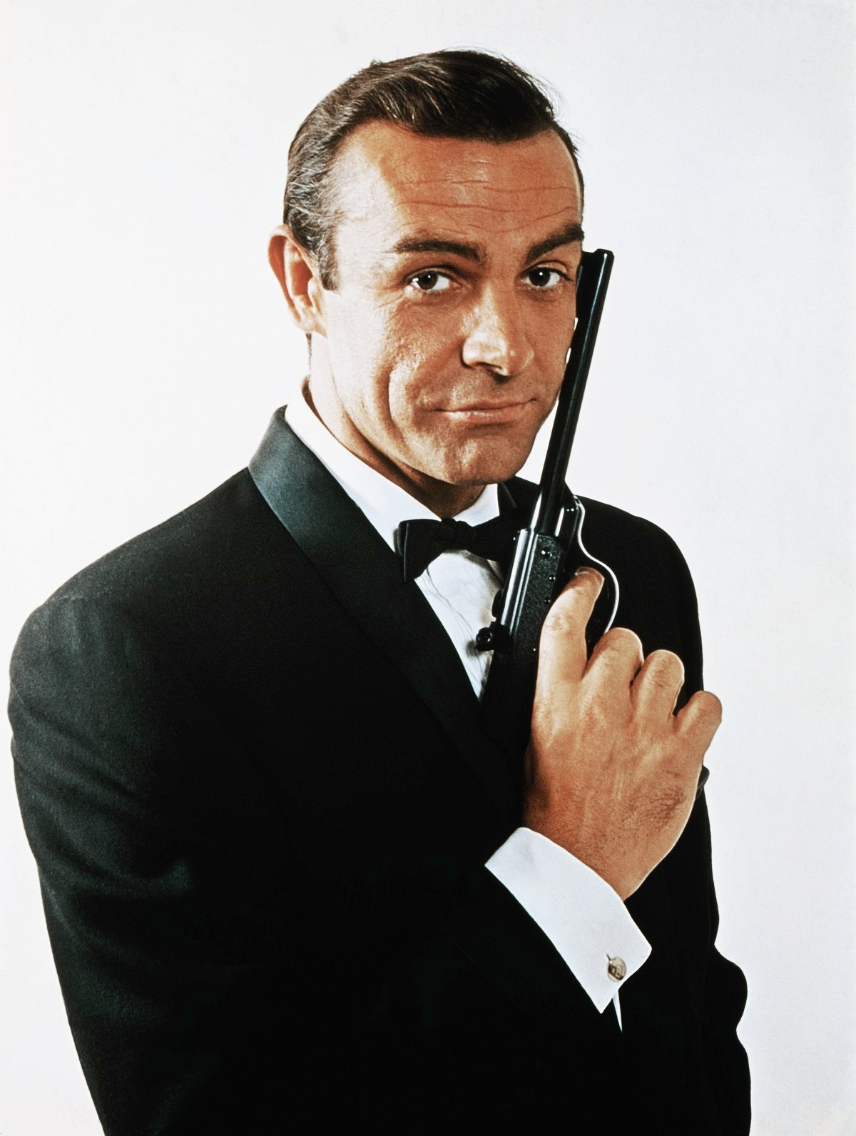 Waist-up portrait of Sean Connery wearing a tuxedo and holding a gun as James Bond
