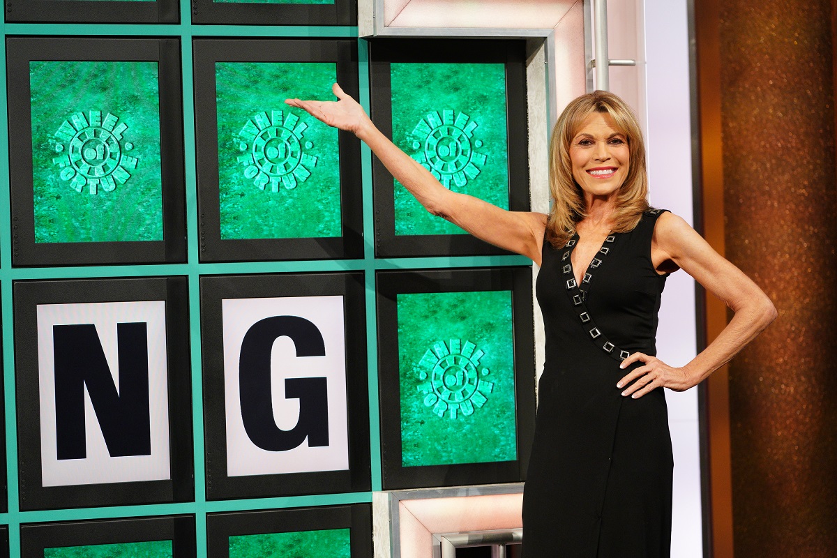 'Wheel of Fortune' host Vanna White wearing a black dress and standing in front of the puzzle board.