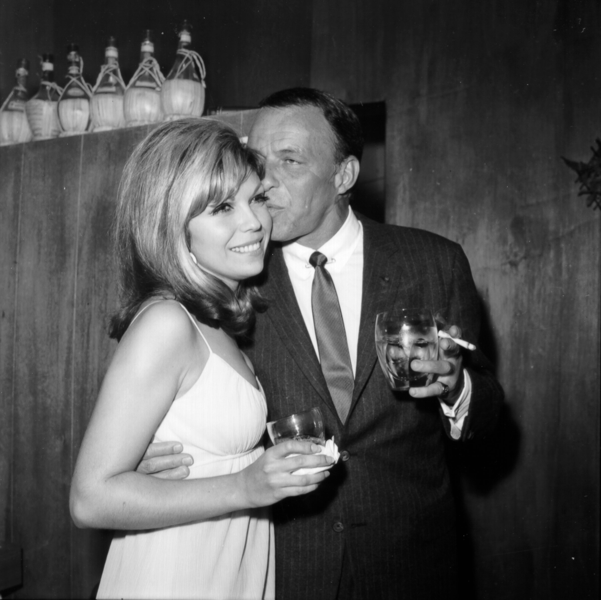 Frank Sinatra kissing his daughter, Nancy Sinatra, near some bottles
