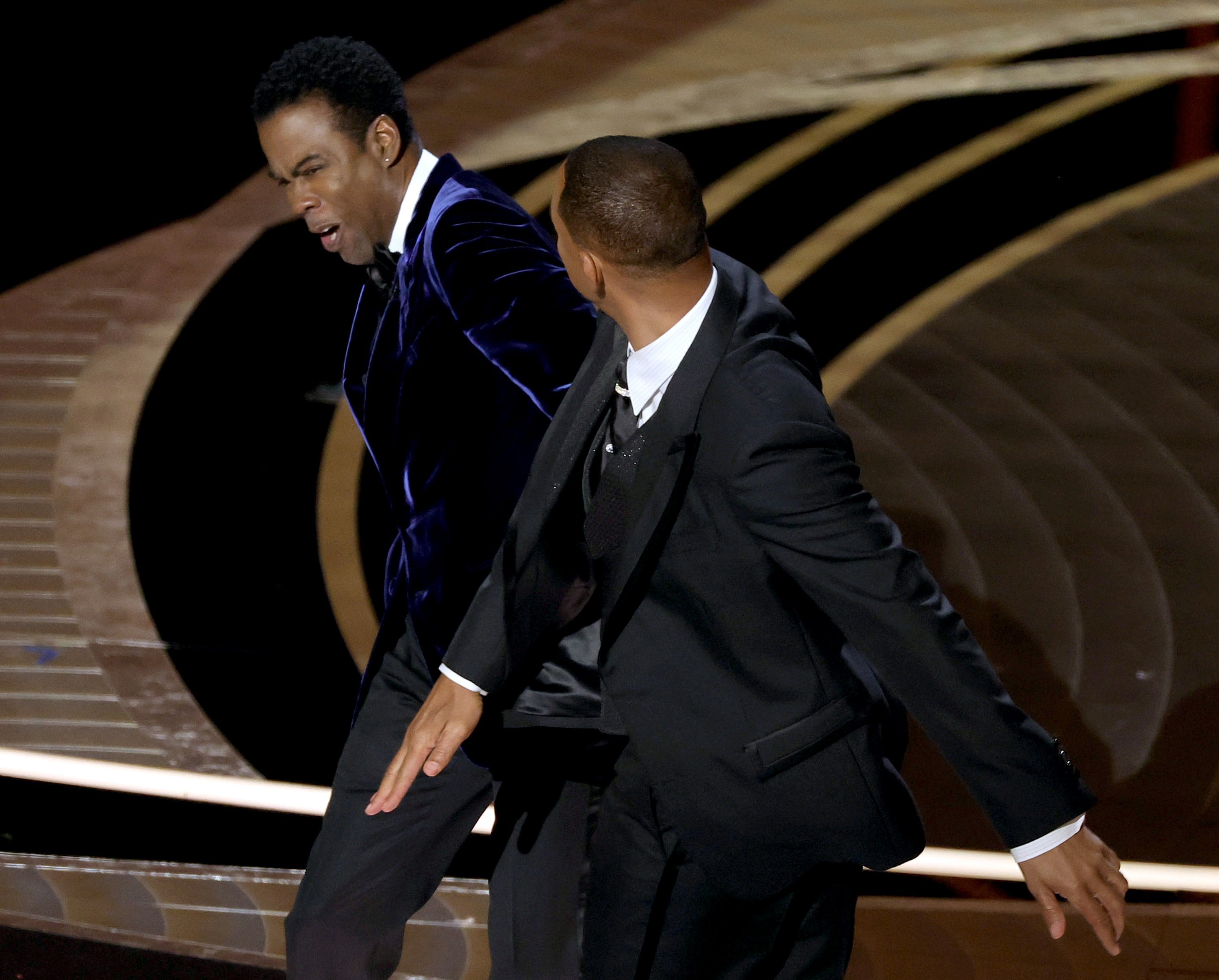 Chris Rock leaning over as Will Smith's hand comes back from hitting the comedian