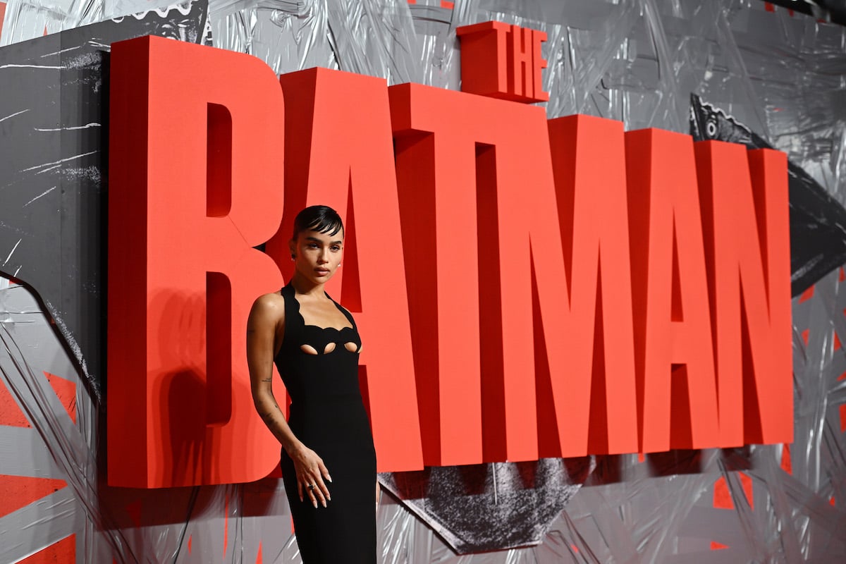 Zoe Kravitz poses in front of a large red sign that says "The Batman."