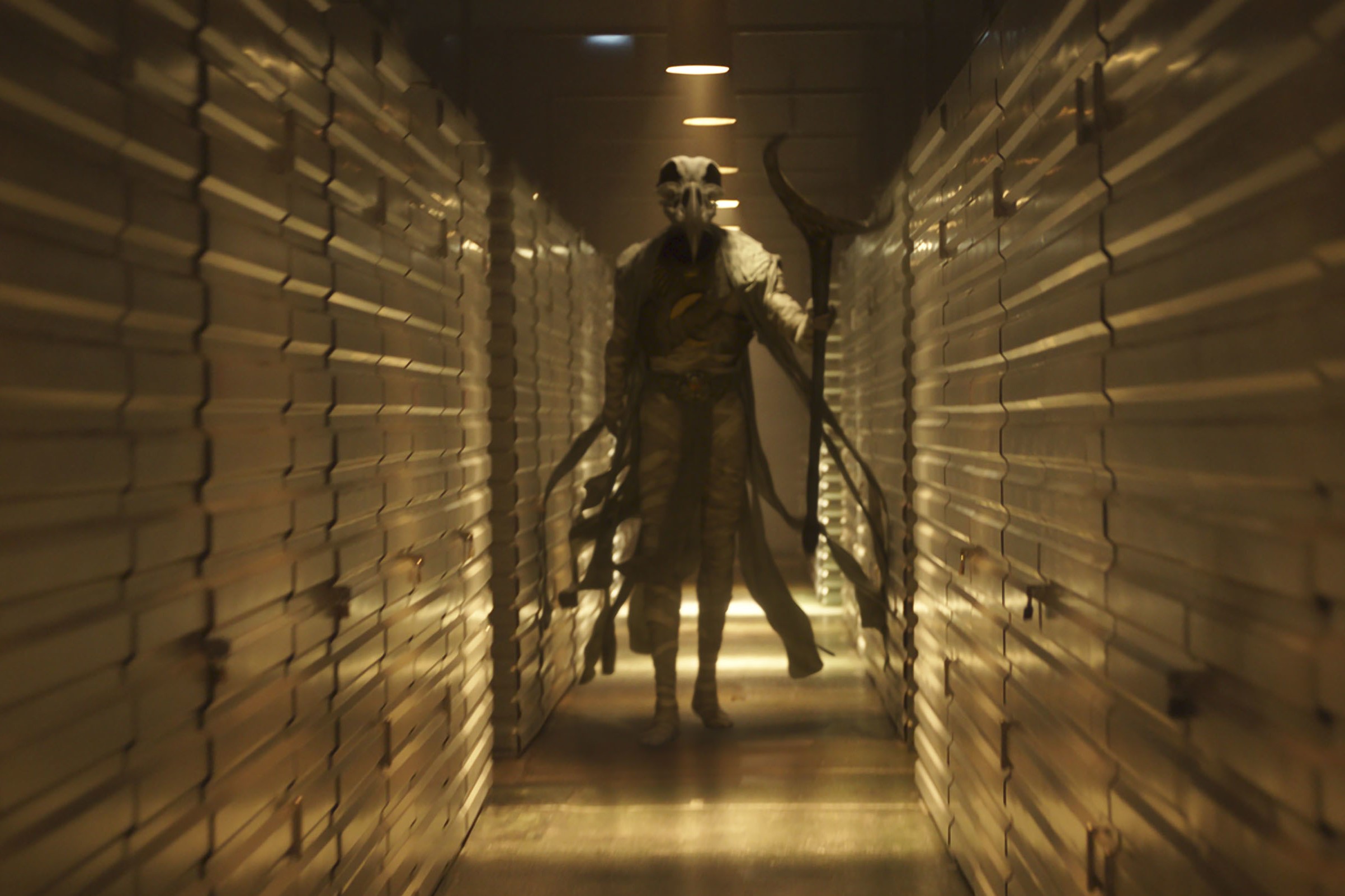 Khonshu, an Egyptian moon god, appears in 'Moon Knight,' and walks down a dimly lit hallway. He is wrapped in pieces of fabric and holds a large staff.