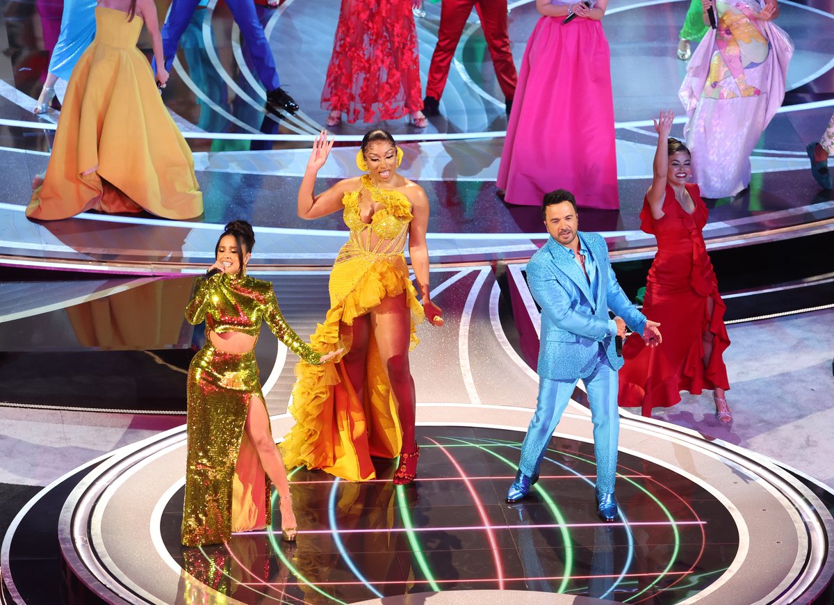 Becky G, Megan Thee Stallion and Luis Fonsi stand on stage wearing bright colors during a performance at the 94th Academy Awards in Hollywood, CA