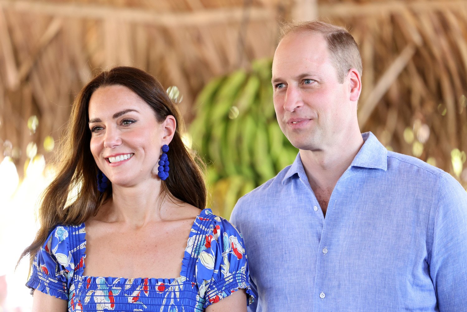 Kate Middleton wears a blue print dress and blue earrings and smiles, Prince William wears a blue button down shirt and smiles while visiting Belize
