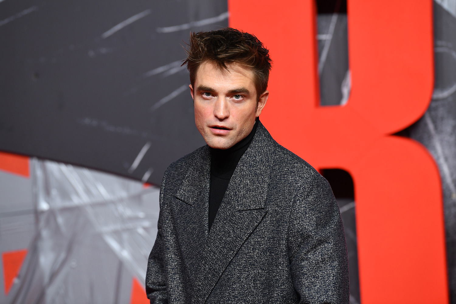 The Batman star Robert Pattinson, whose Batman villains include the Riddler and Penguin, poses in a gray coat at a screening in London.