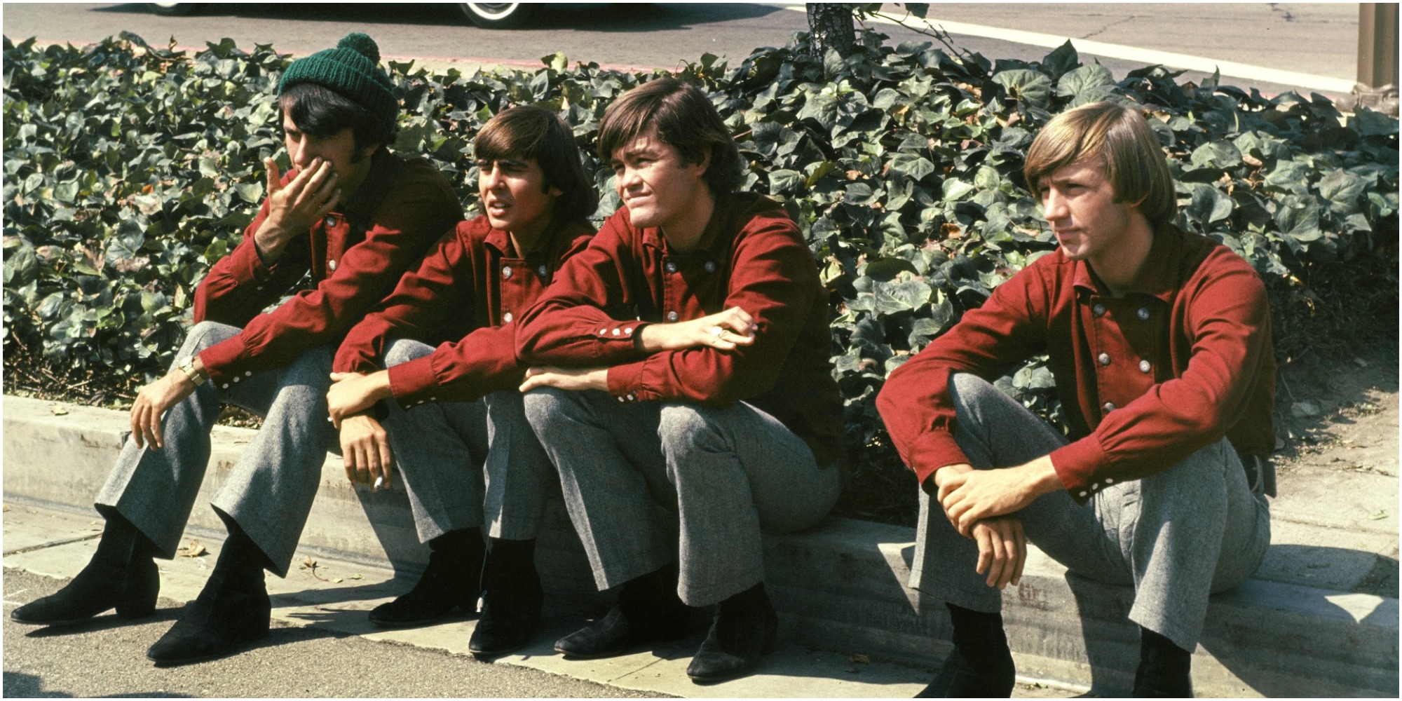 The Monkees cast sit on a curb in a scene of the series.