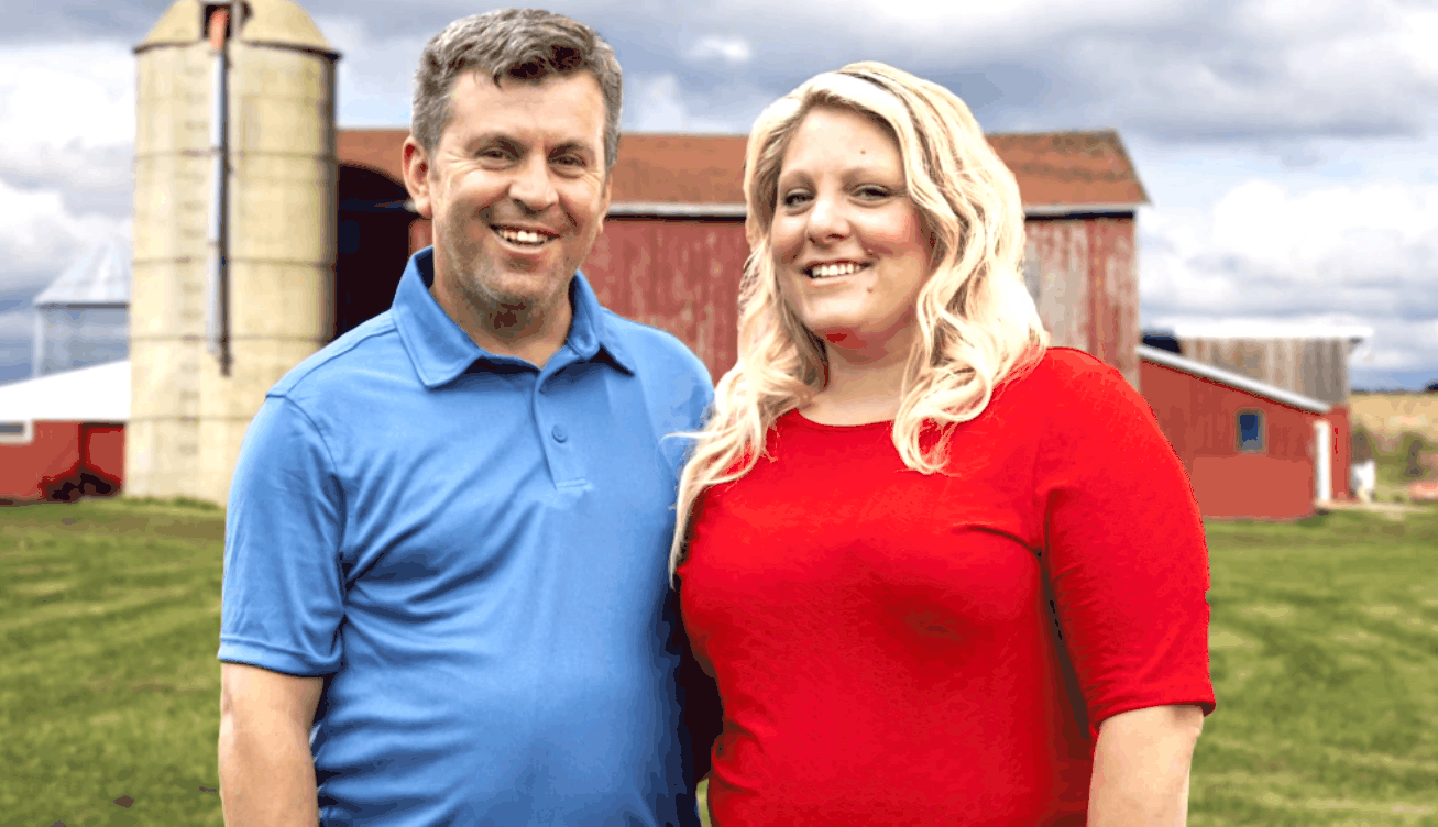 Anna-Marie Campisi and Mursel Mistanoglu standing together in front of a farm background in Nebraska for '90 Day Fiancé' Season 7 promo.