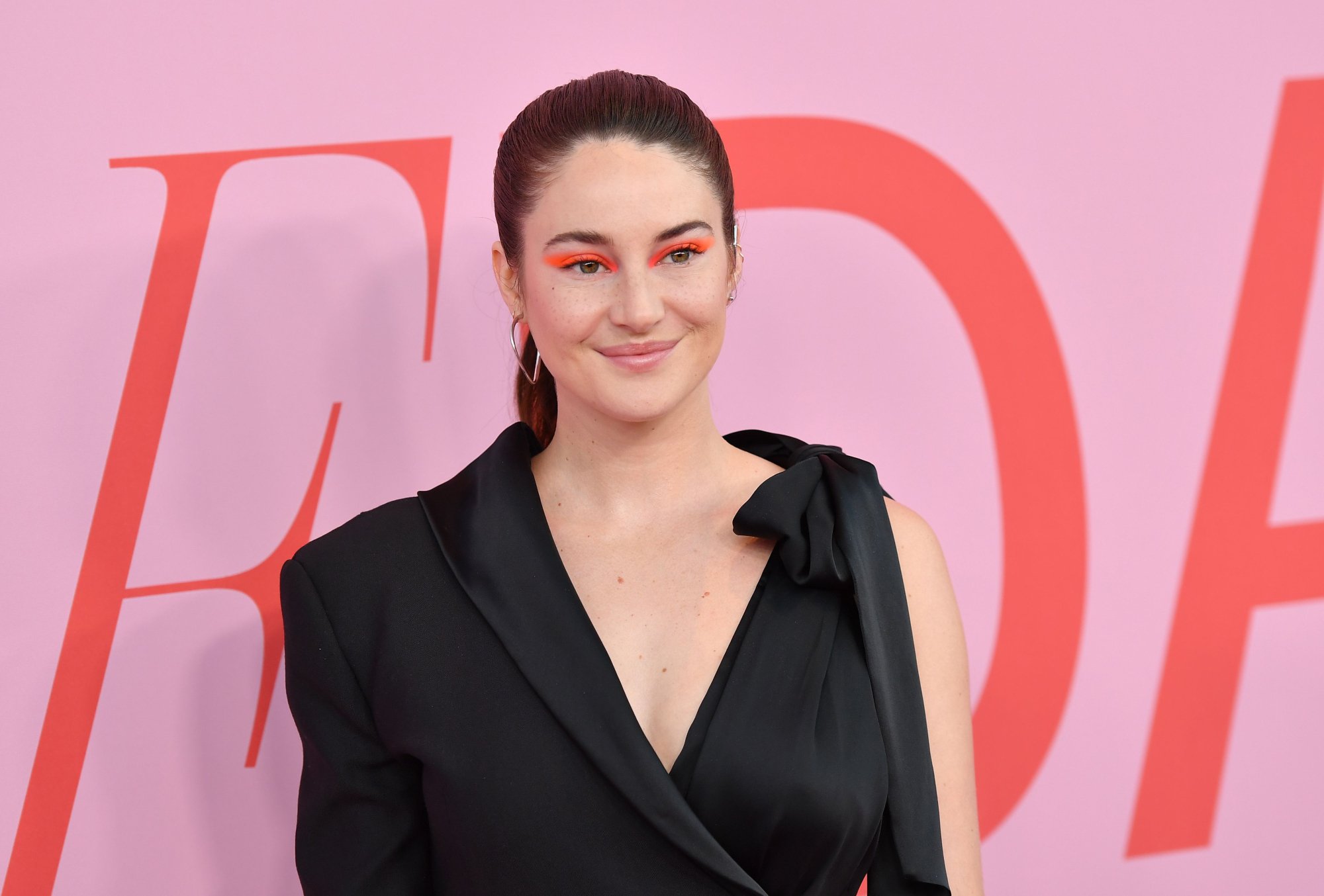 Actor Shailene Woodley, ex of Aaron Rodgers, wearing a black dress in front of a pink step and repeat