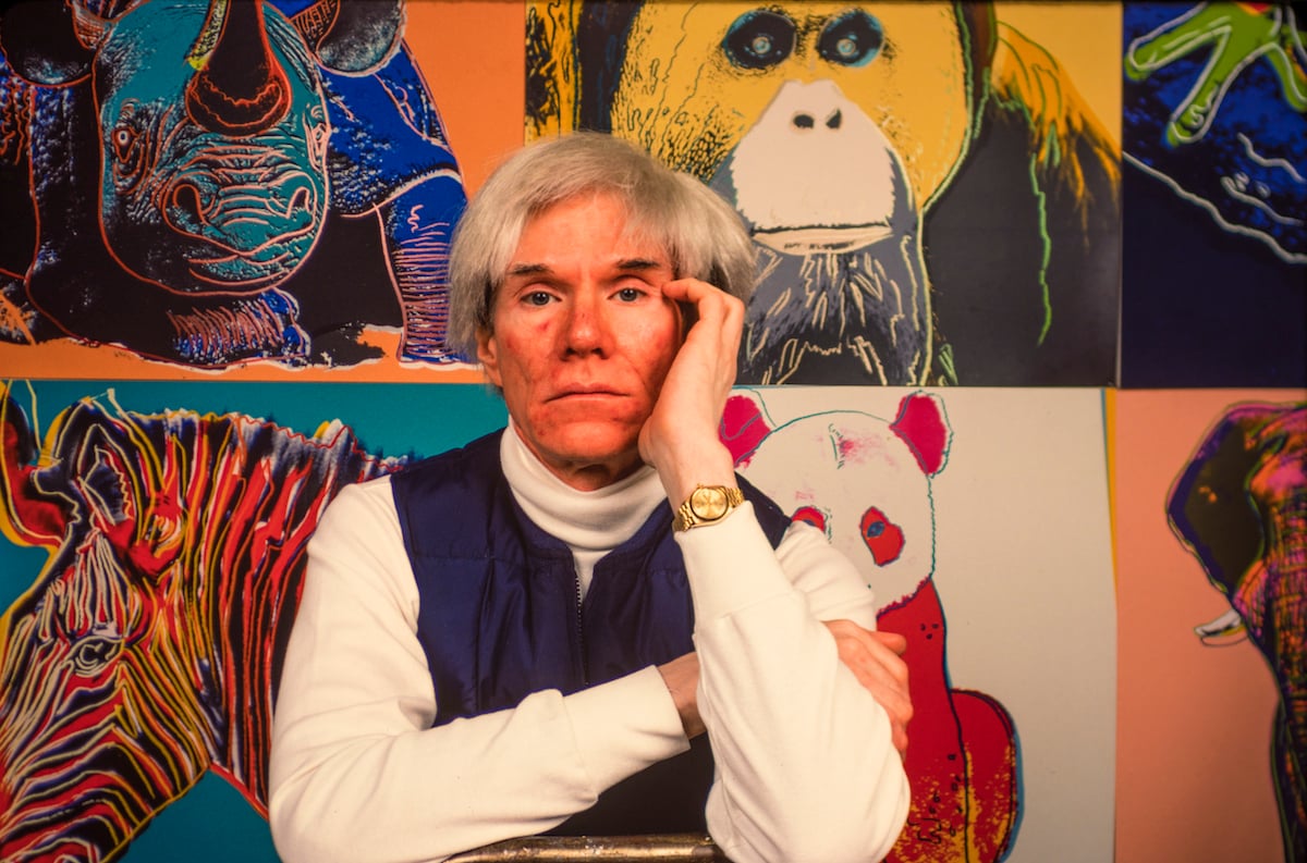 American pop artist Andy Warhol sits in front of several paintings in his 'Endangered Species' series in 1983