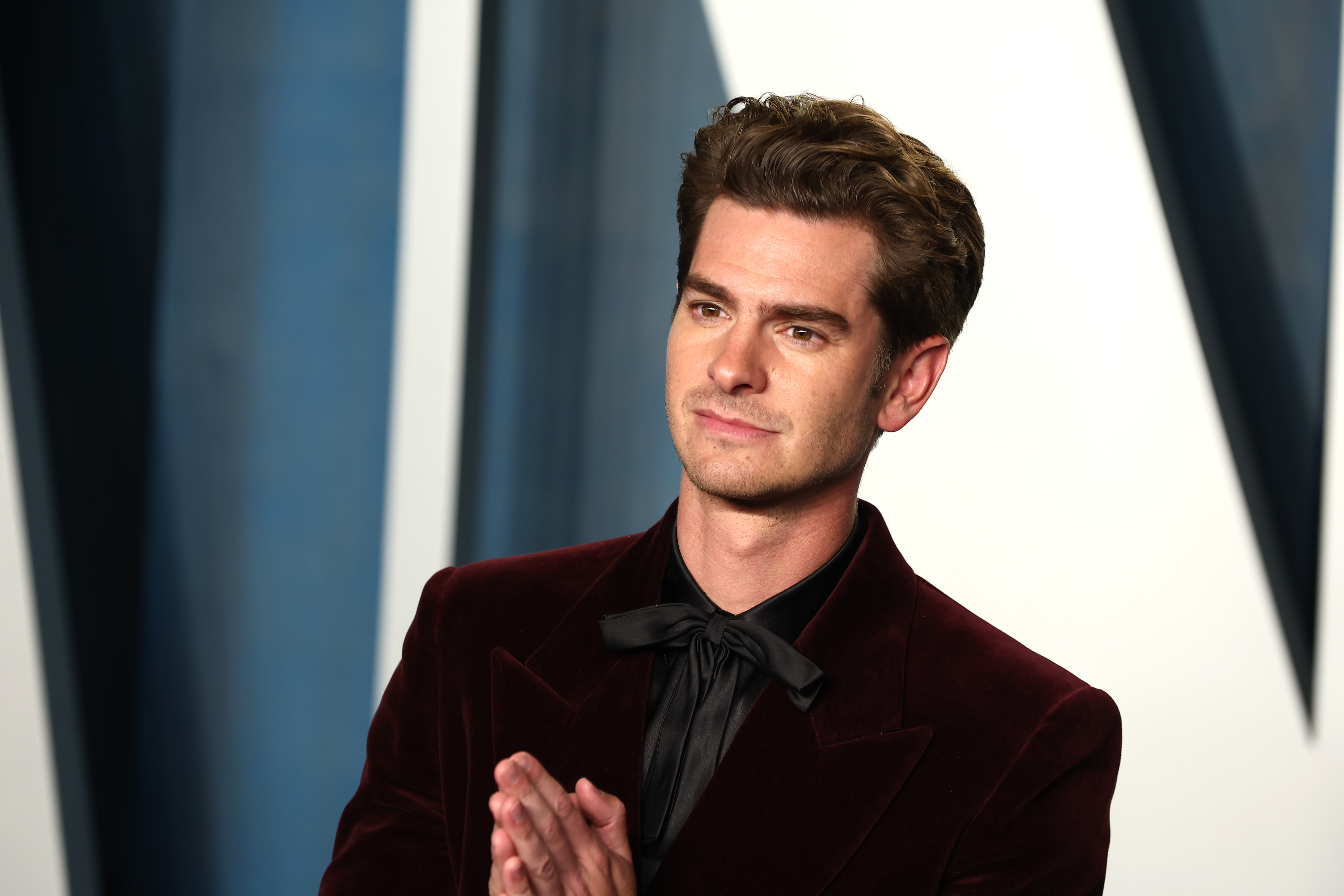 Andrew Garfield, star of 'Spider-Man: No Way Home,' wears a dark red velvet suit over a black button-up shirt and black tie.