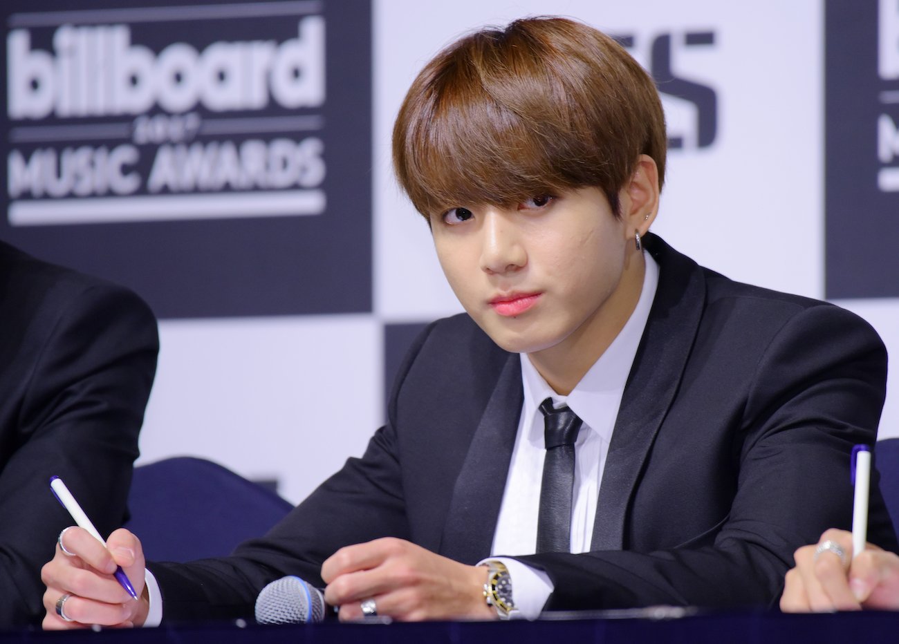 BTS member Jungkook wearing a suit and looking on in front of a black-and-white background