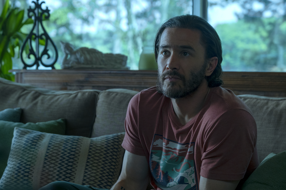Tom Pelphrey wears a red graphic tee with his hair slicked back in a scene from the Netflix show 'Ozark' as Ben Davis