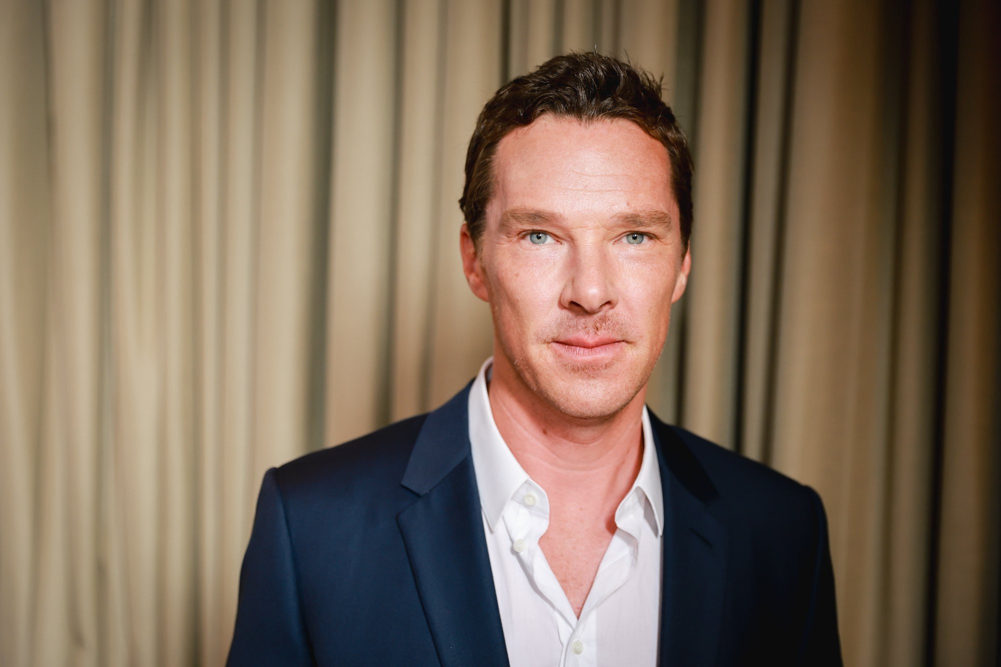 'Doctor Strange 2' star Benedict Cumberbatch. He's wearing a white button-up shirt and blue jacket and standing in front of a light brown curtain.