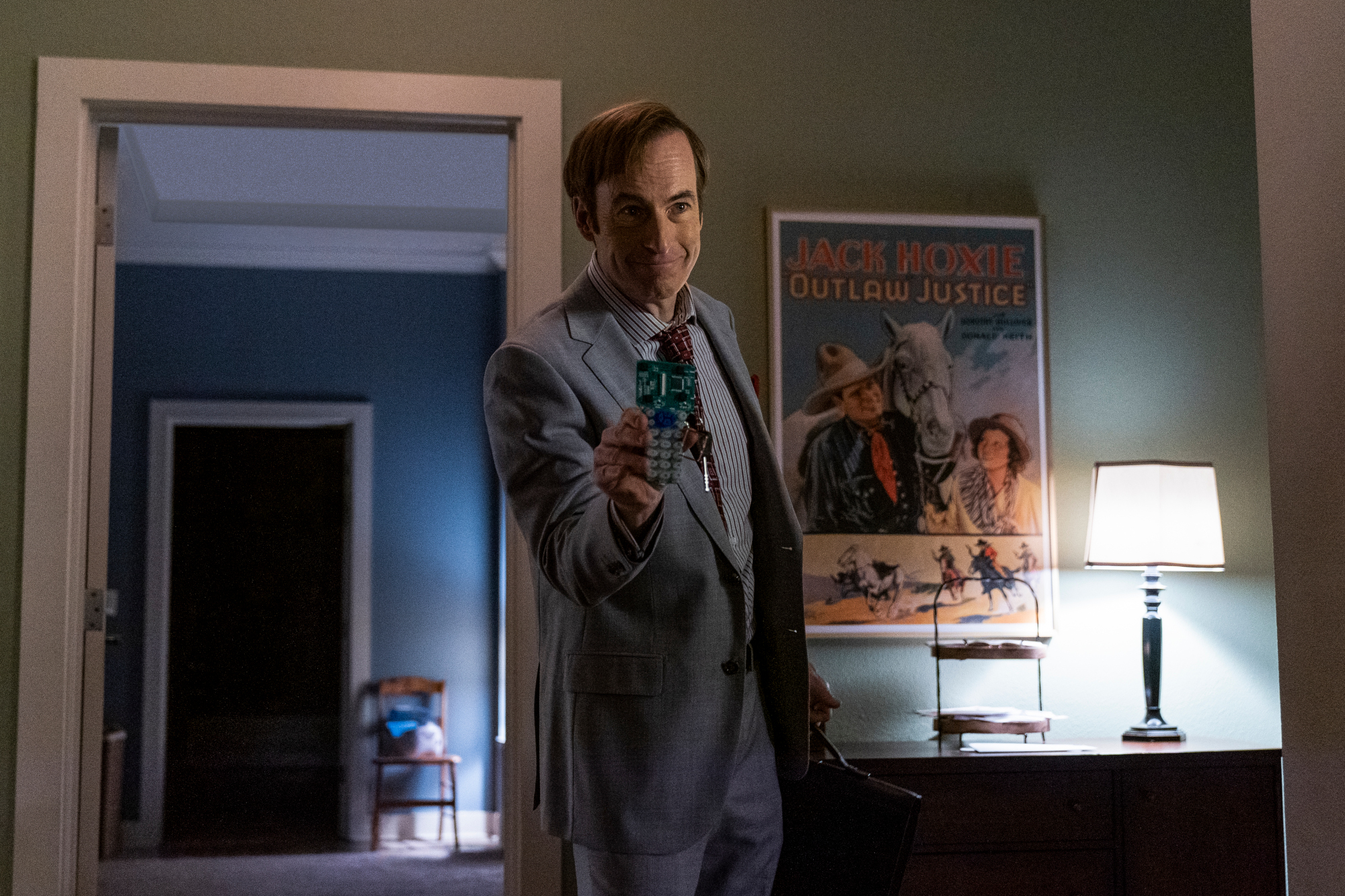 Bob Odenkirk as Saul Goodman in 'Better Call Saul' Season 6 Episode 3. He's standing in front of a doorway and holding out some type of chip.